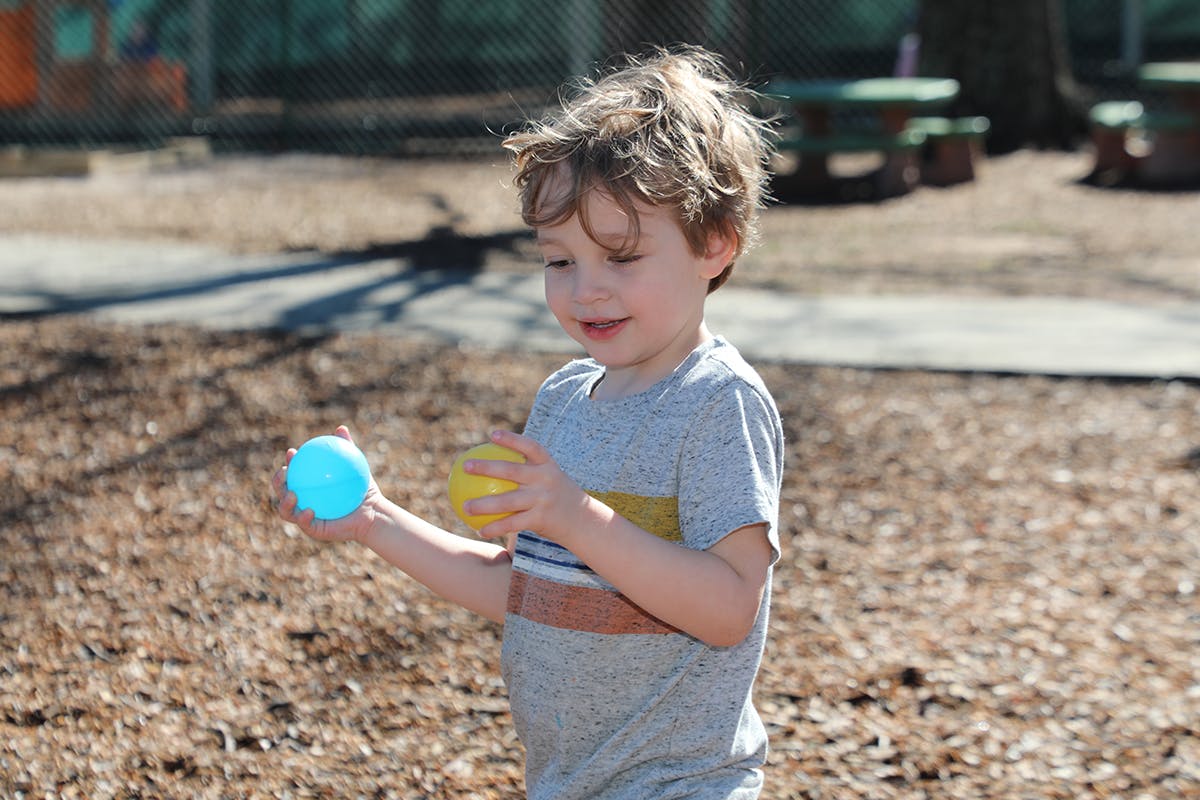 Child holding a blue ball in one hand and a yellow ball in the other