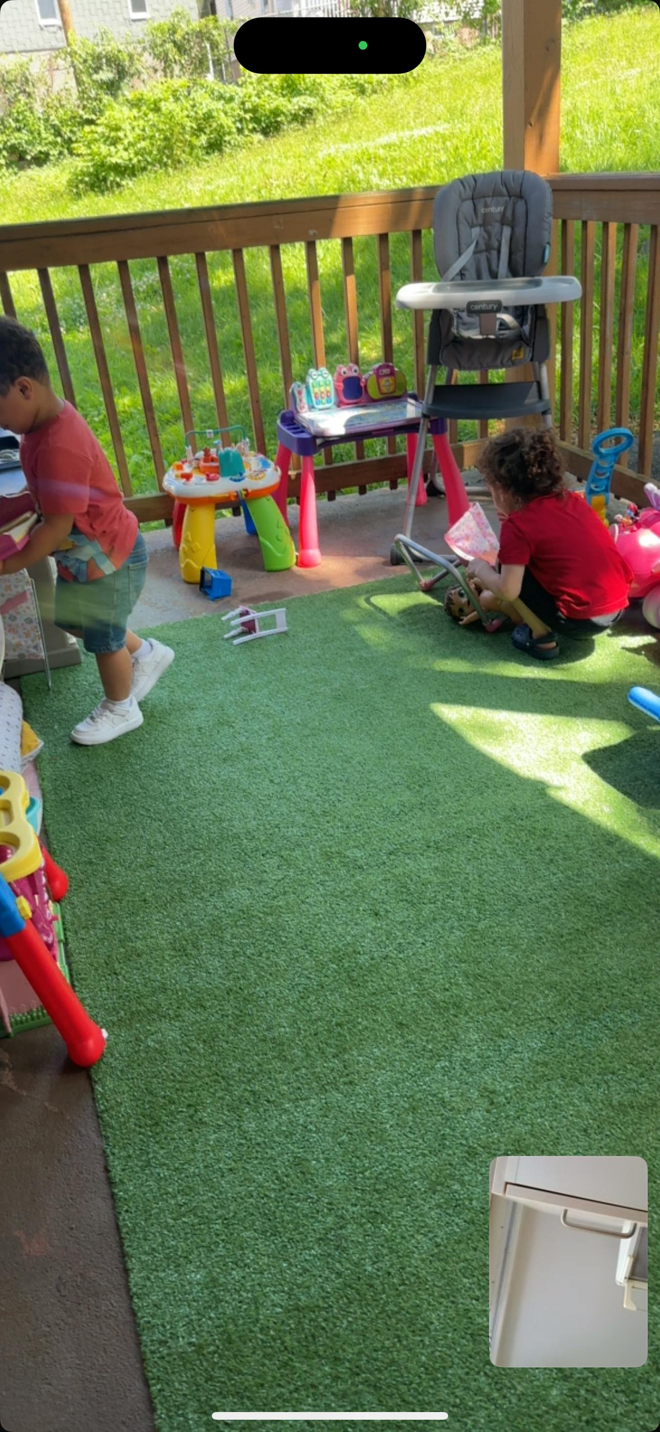 Two children playing with toys on a patio with artificial grass