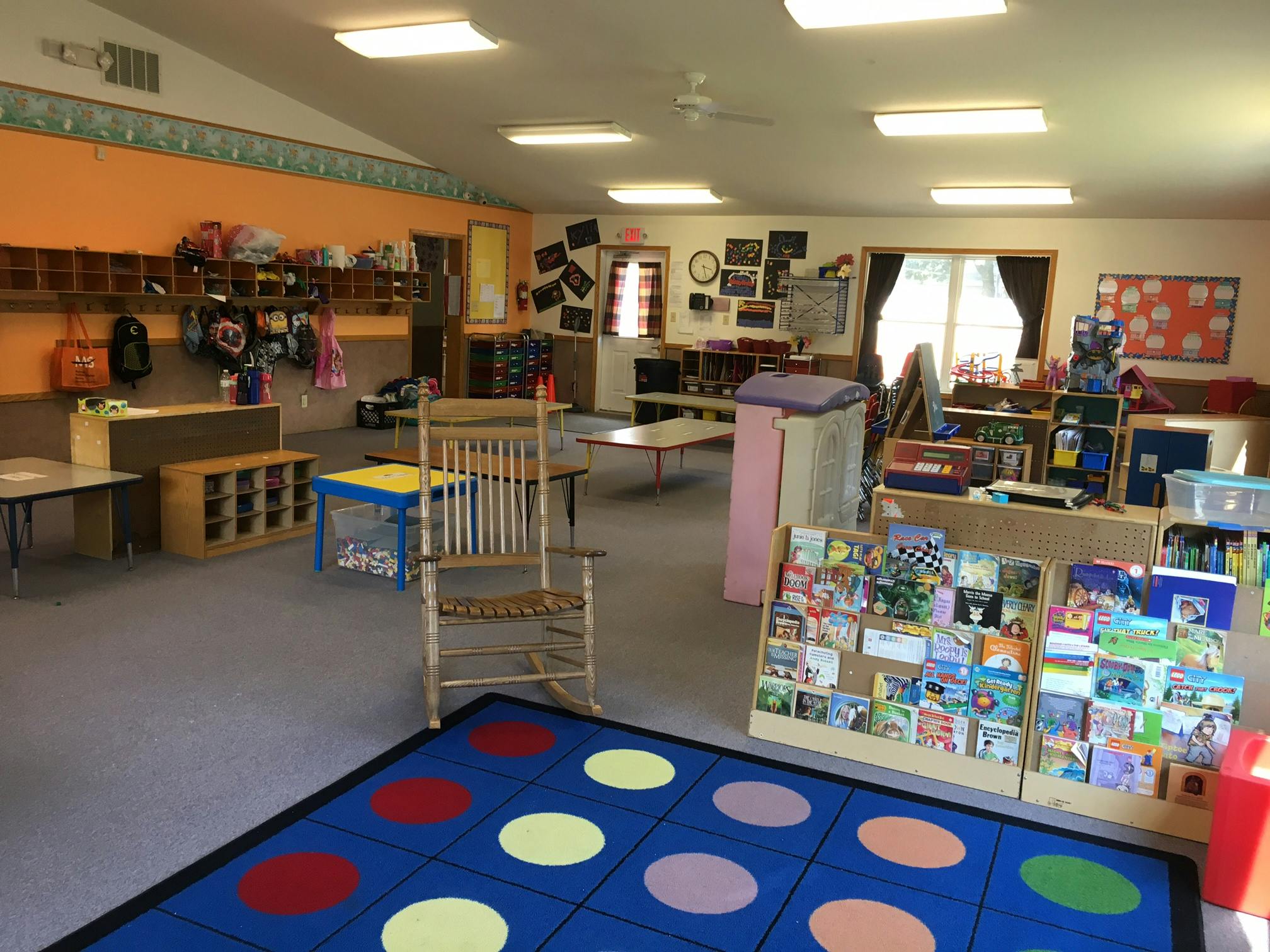 Classroom with a blue rug with colorful circles, tables, and shelves