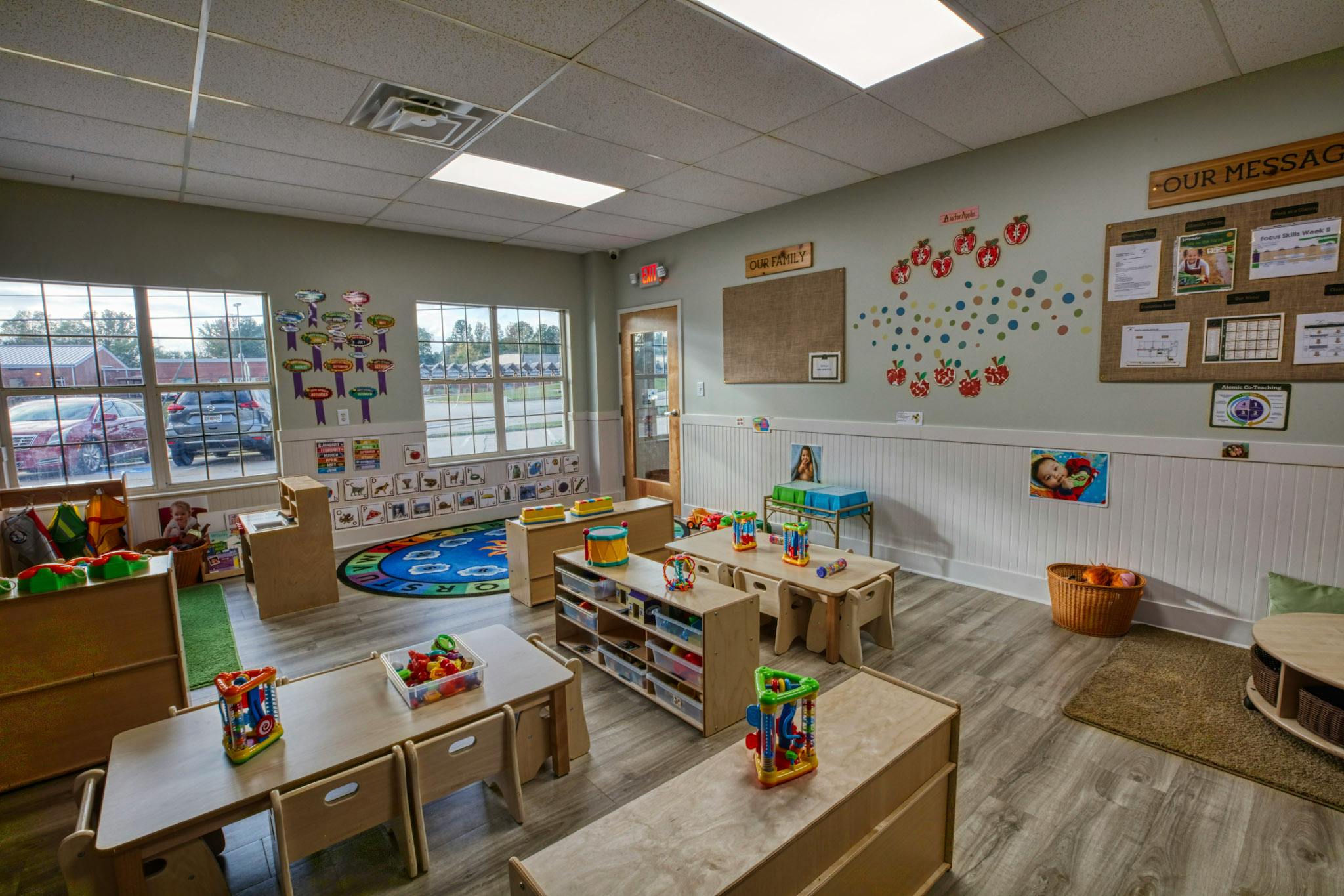An empty childcare classroom with small tables and chairs, toys, and educational wall decor