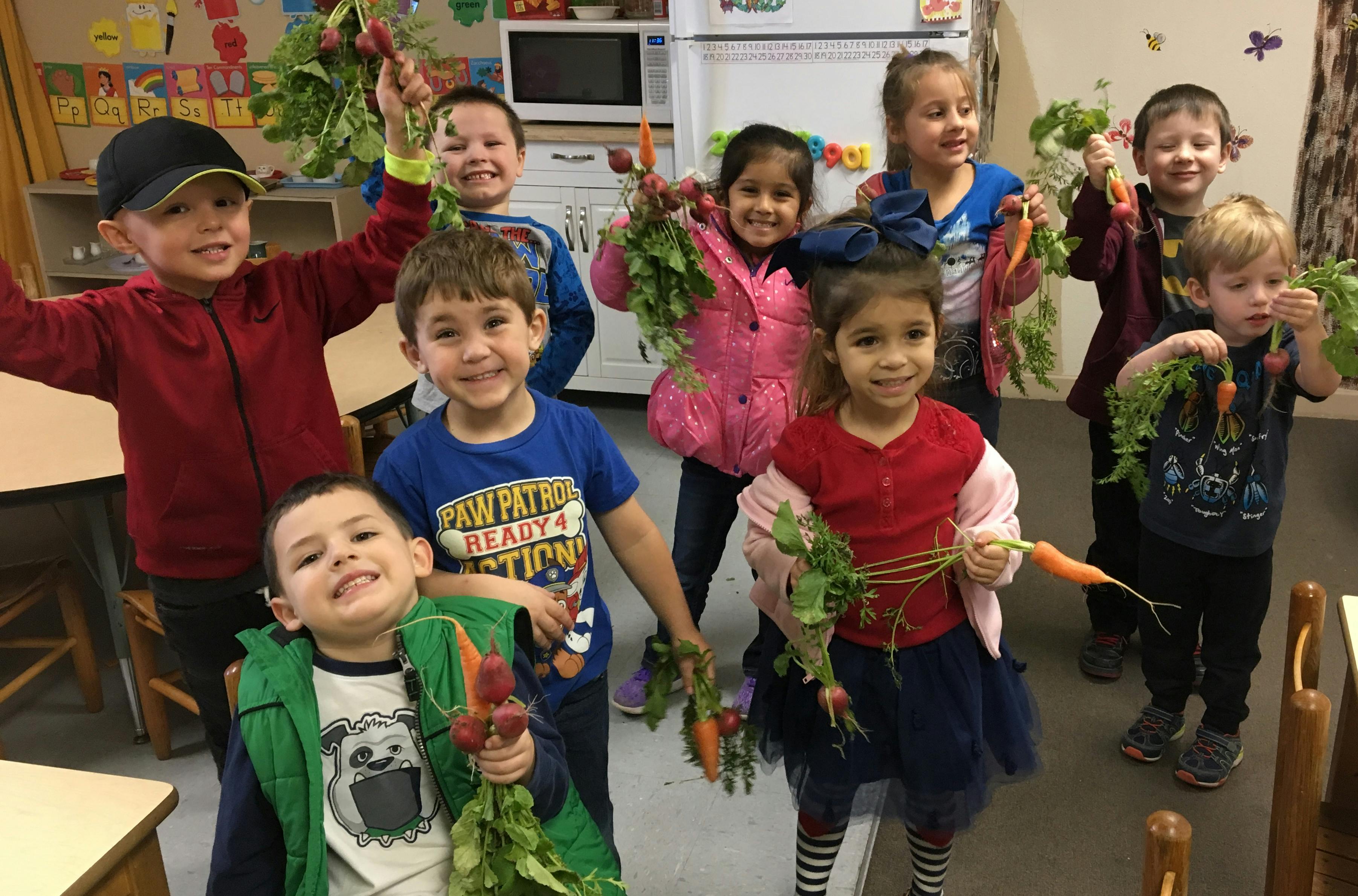 Group of children holding freshly harvested carrots and radishes