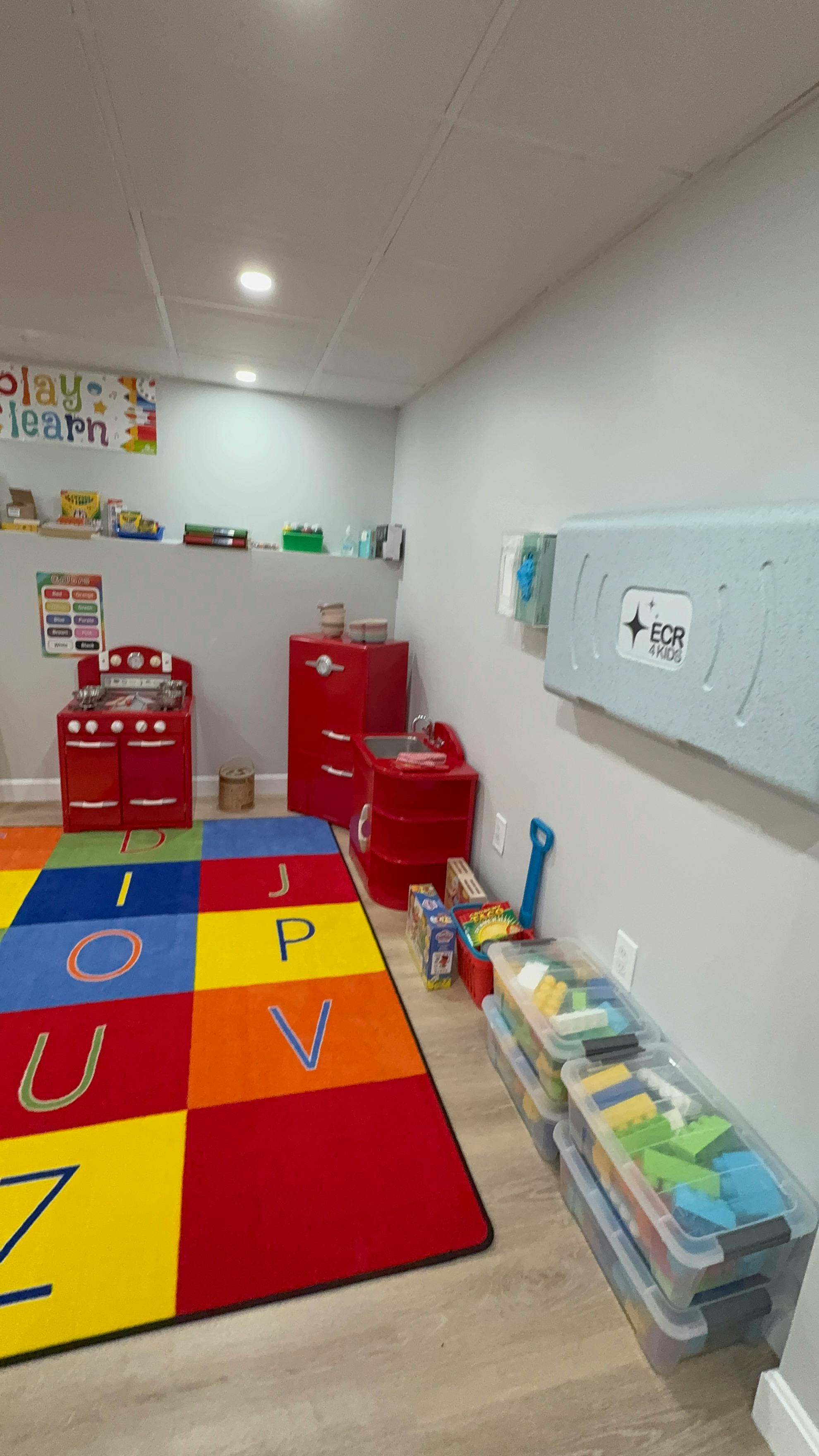 Playroom with a colorful alphabet rug, toy kitchen, and storage bins