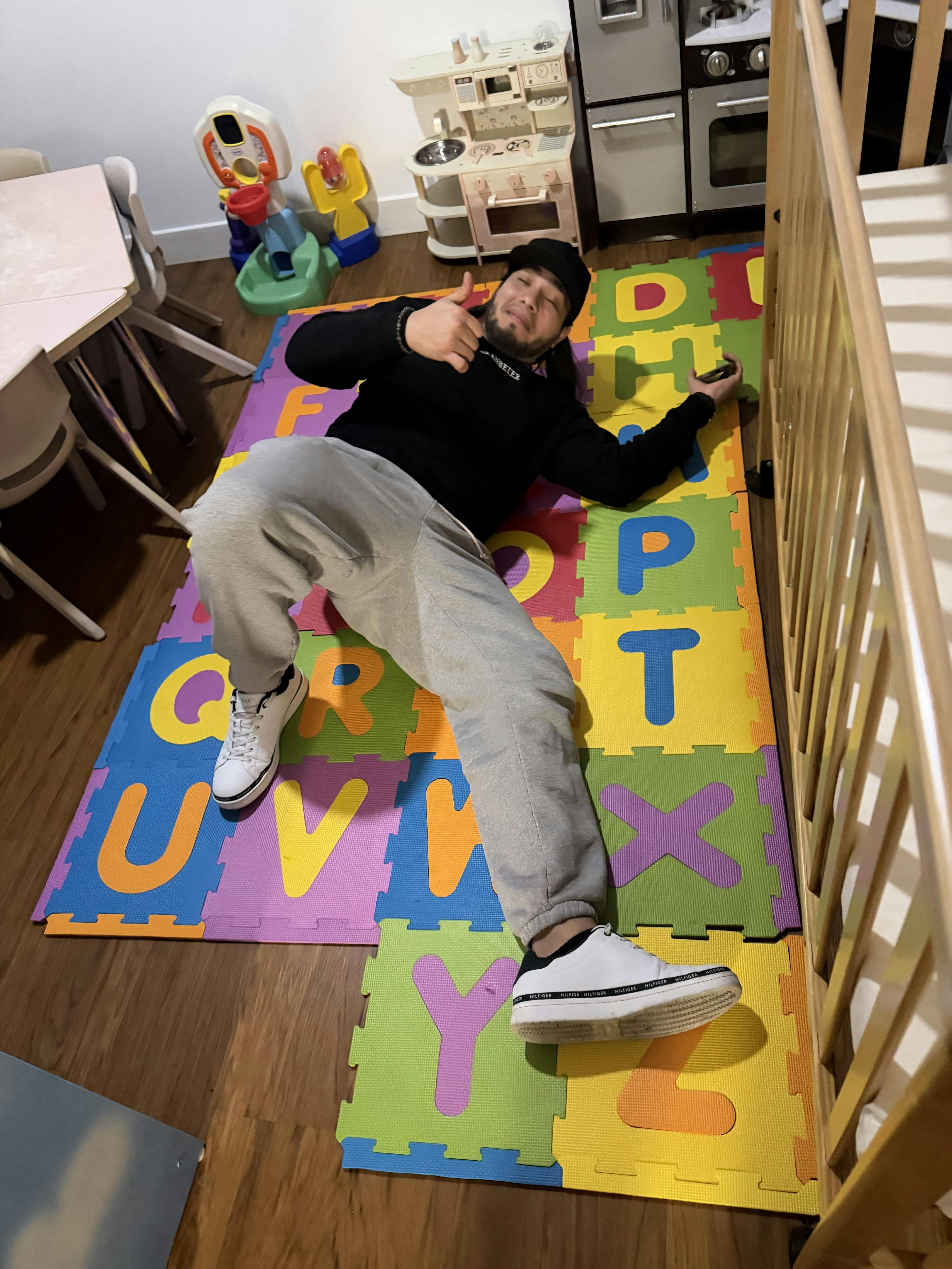 Person laying on alphabet playmats, holding a phone and giving a thumbs up