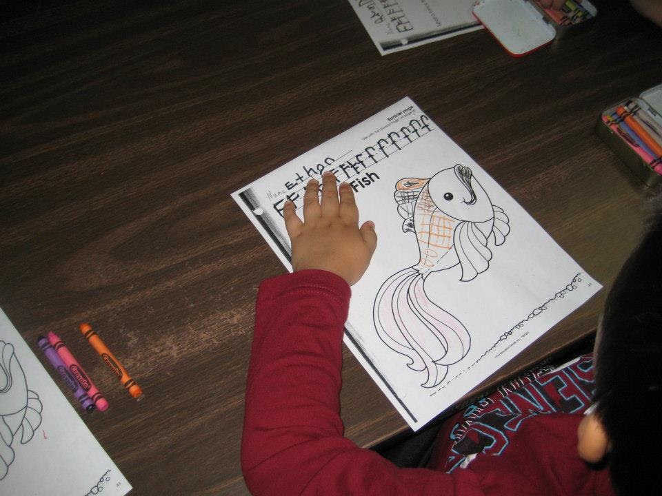 Child's hand on a coloring page with a fish drawing and the word "Fish"
