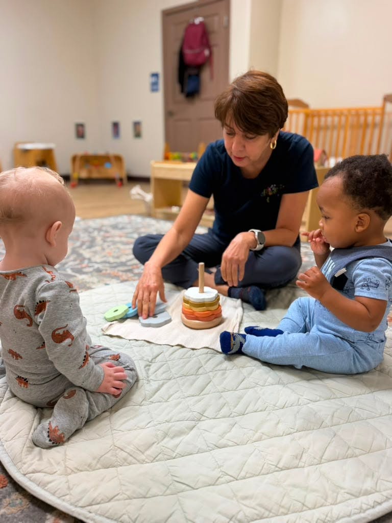 Adult sitting on the floor playing with two children using stacking rings