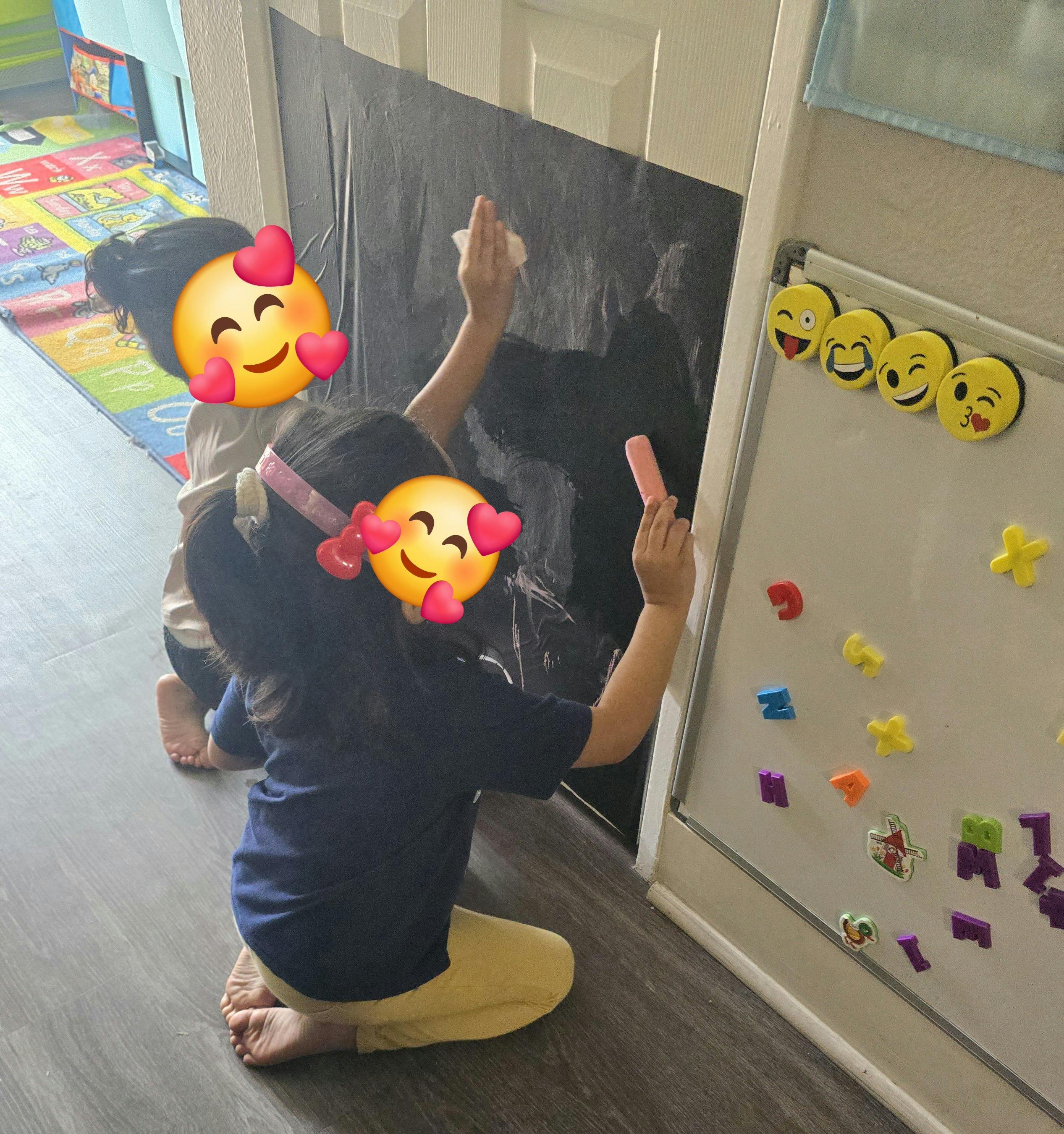 Two children kneeling and drawing on a chalkboard on a door