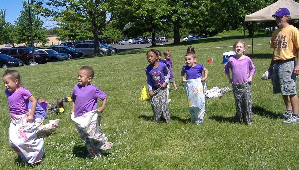 Children participating in a sack race outdoors with an adult observing