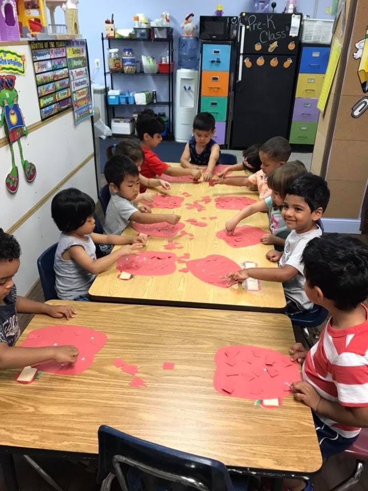 Children at tables in a classroom doing an activity with red paper cutouts
