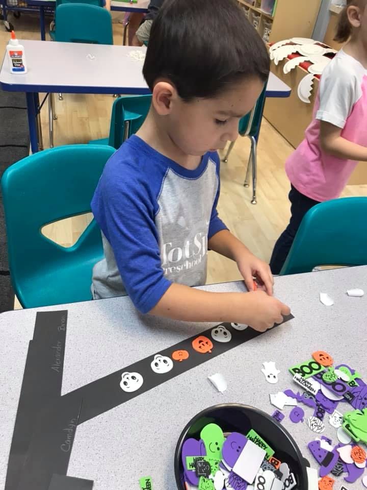 Child decorating a black paper strip with pumpkin and ghost cutouts