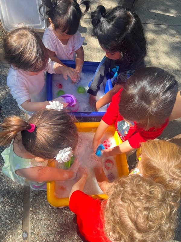 Children playing with water and bubbles in plastic bins