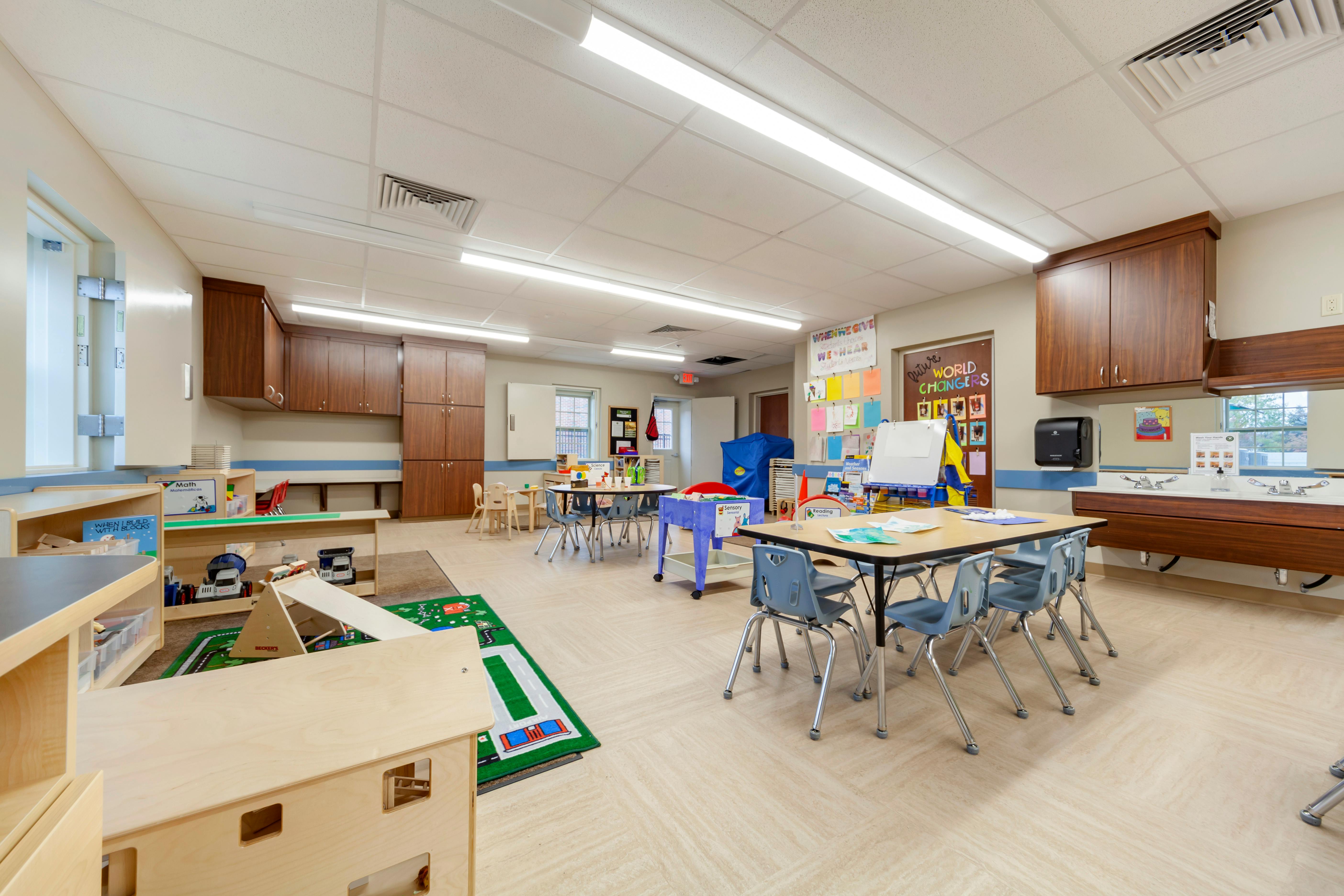 An empty early childhood classroom with play areas, tables, and chairs