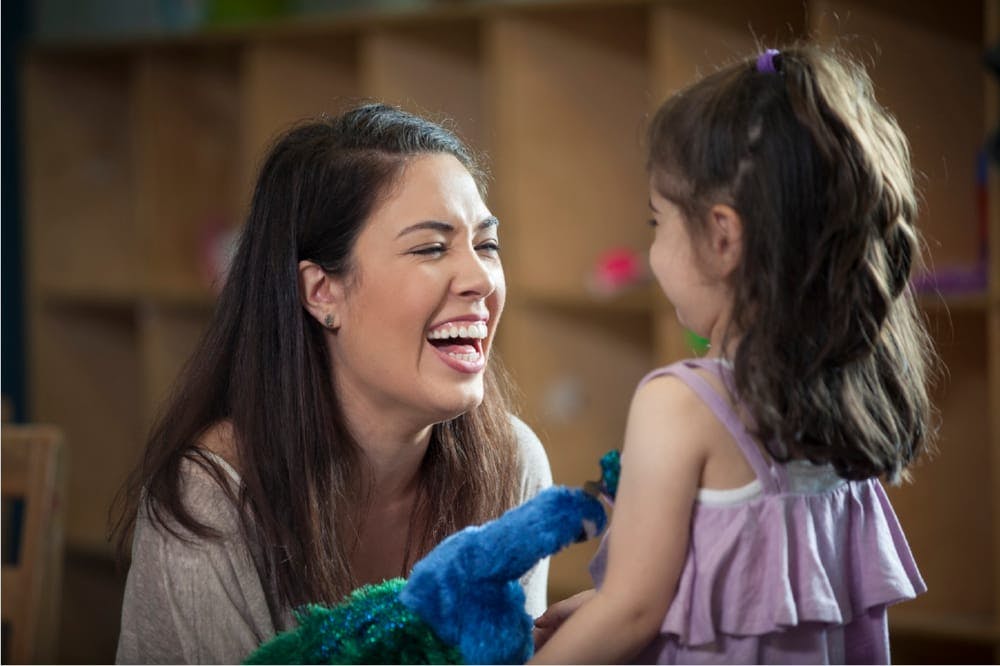 Person laughing with a child holding a blue puppet