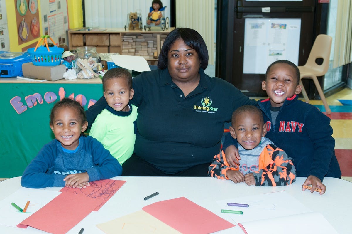 Adult and four children sitting at a table with paper and paper and paper