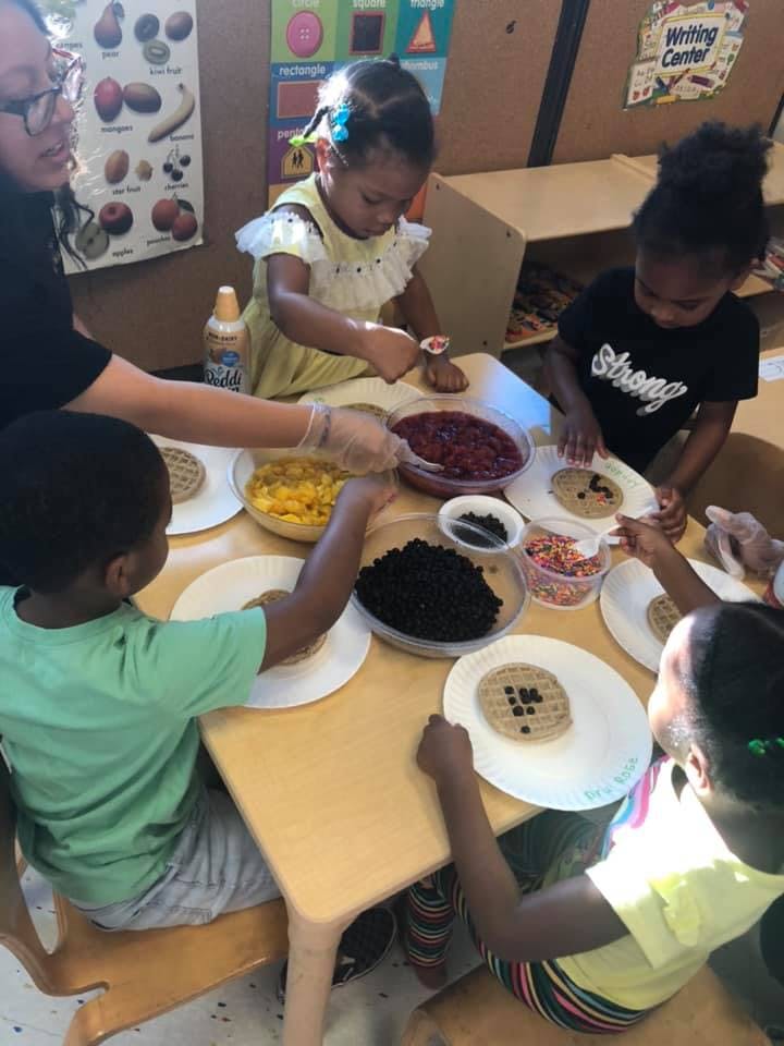 Adult and children decorating waffles with toppings at a table