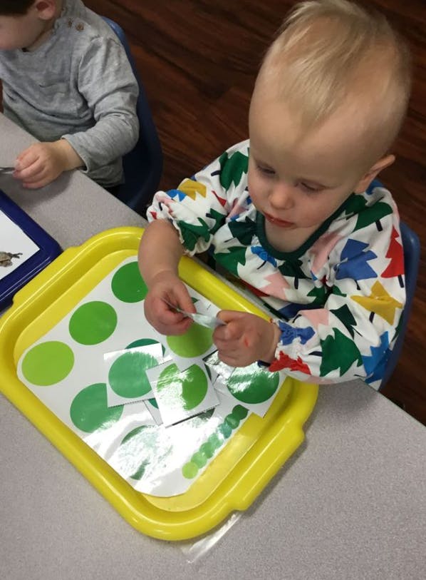 Child peeling green circle stickers from a sheet on a yellow tray