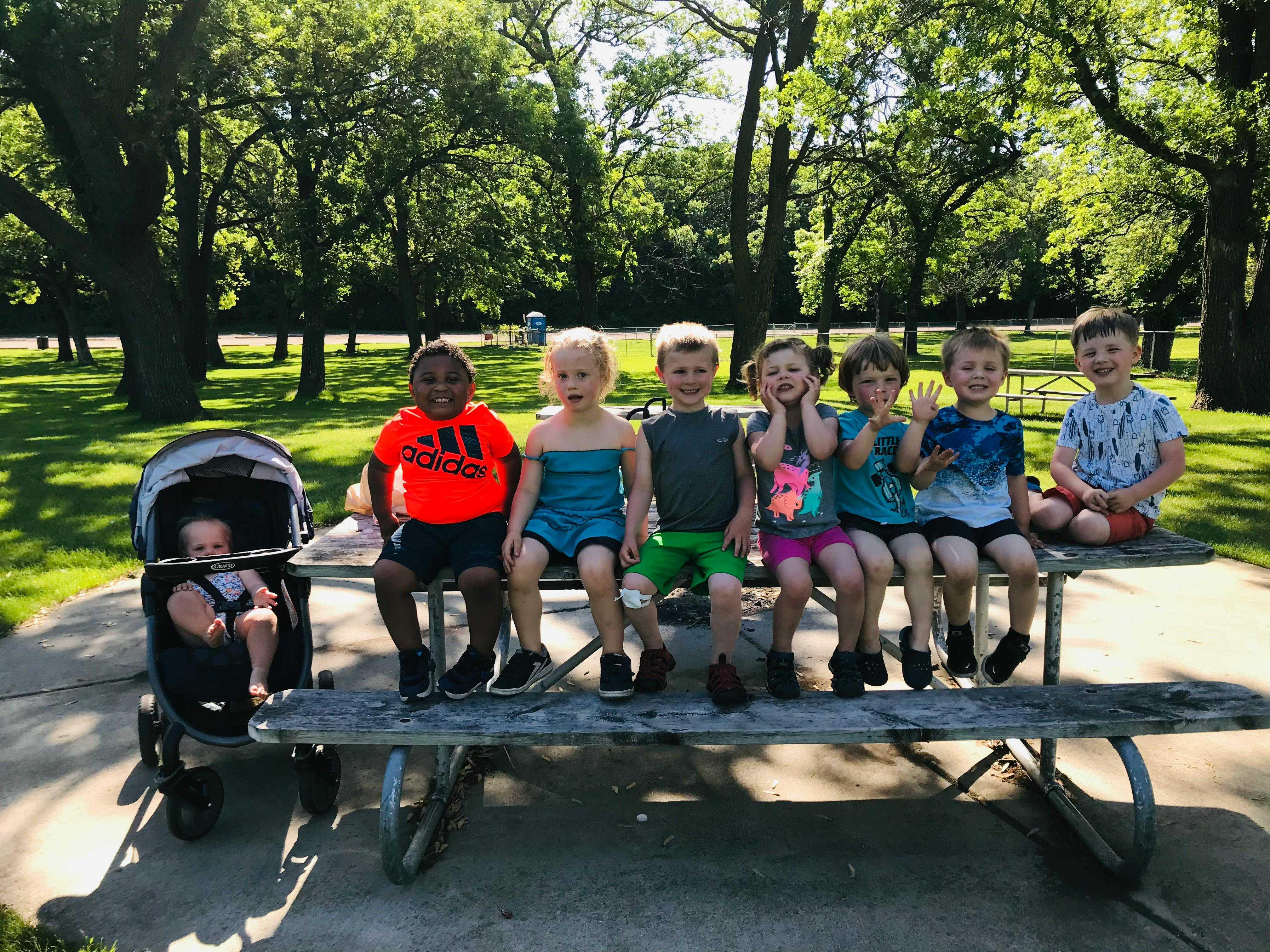 Children and a baby in a stroller sitting on a picnic table outdoors