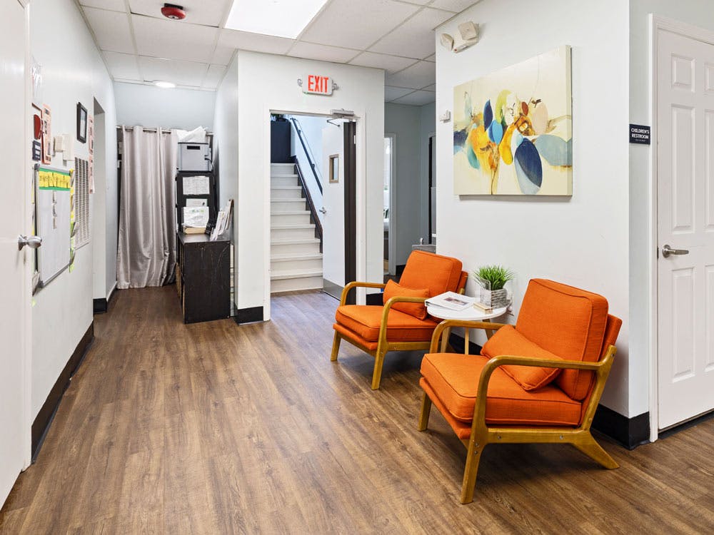 Waiting area with two orange chairs, a small table, and an abstract painting