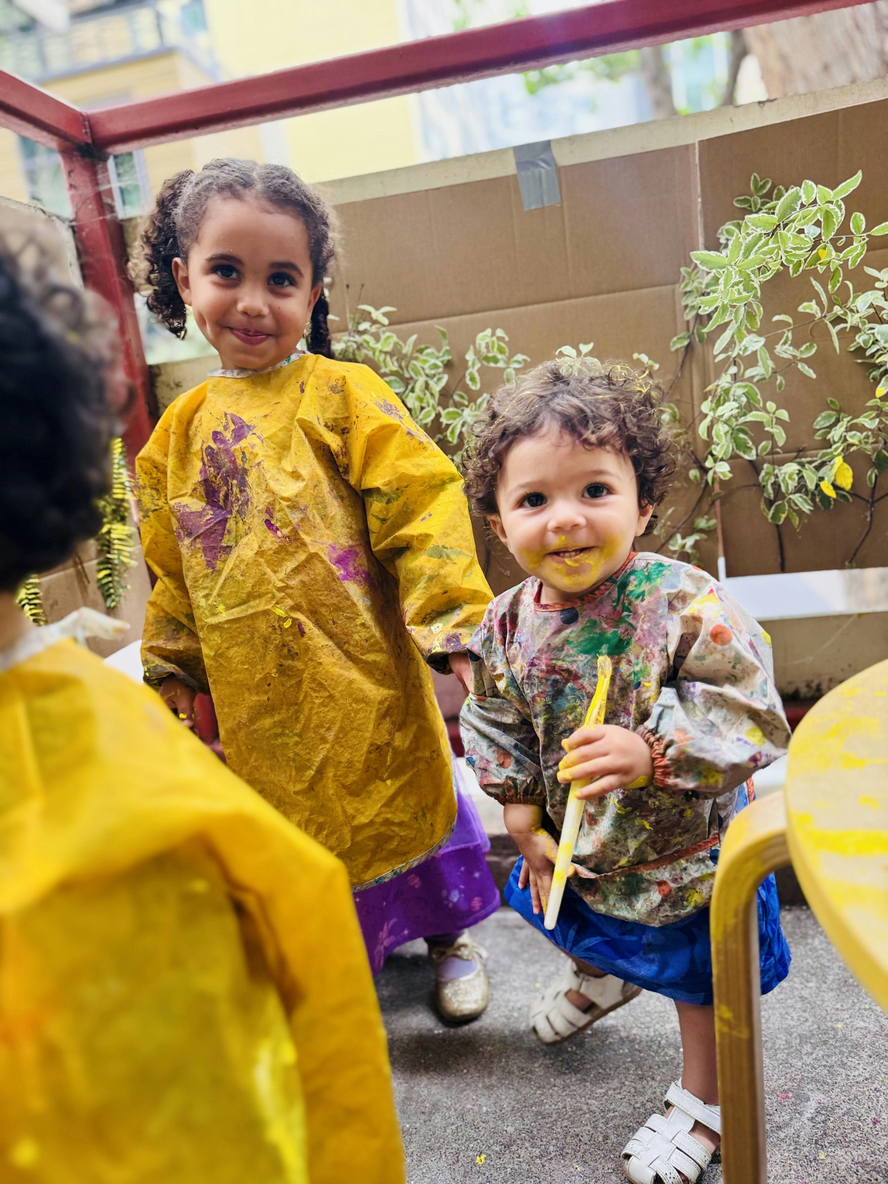 Two children in paint-splattered smocks, one holding a paintbrush