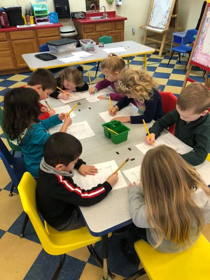 Children sitting at a table, writing on papers with pencils