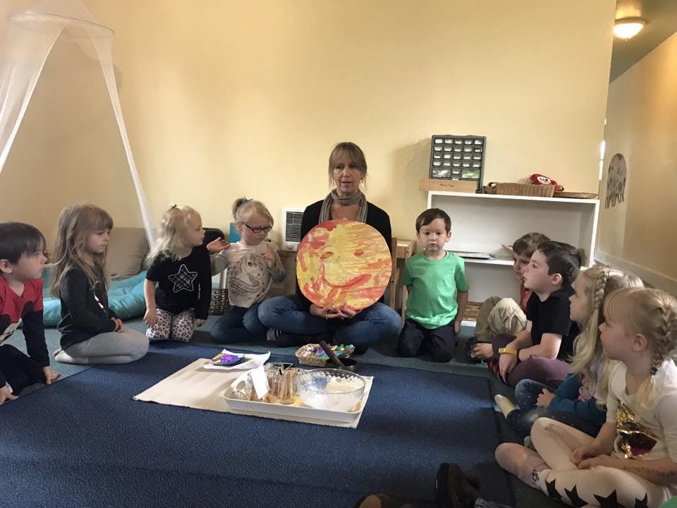 Person holding a large round object with children sitting around them in a classroom