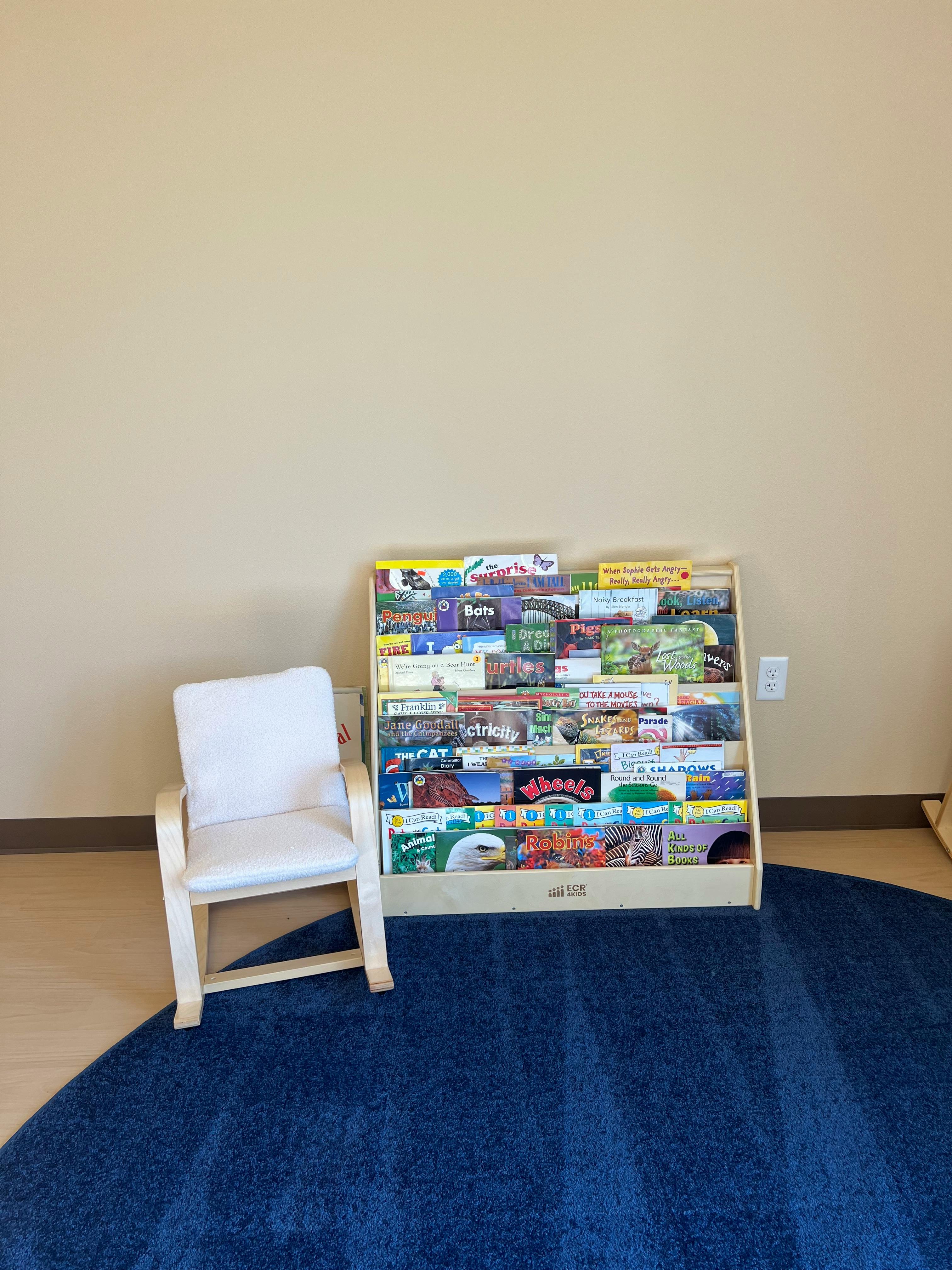 Small white chair next to a bookshelf filled with children's books on a blue rug