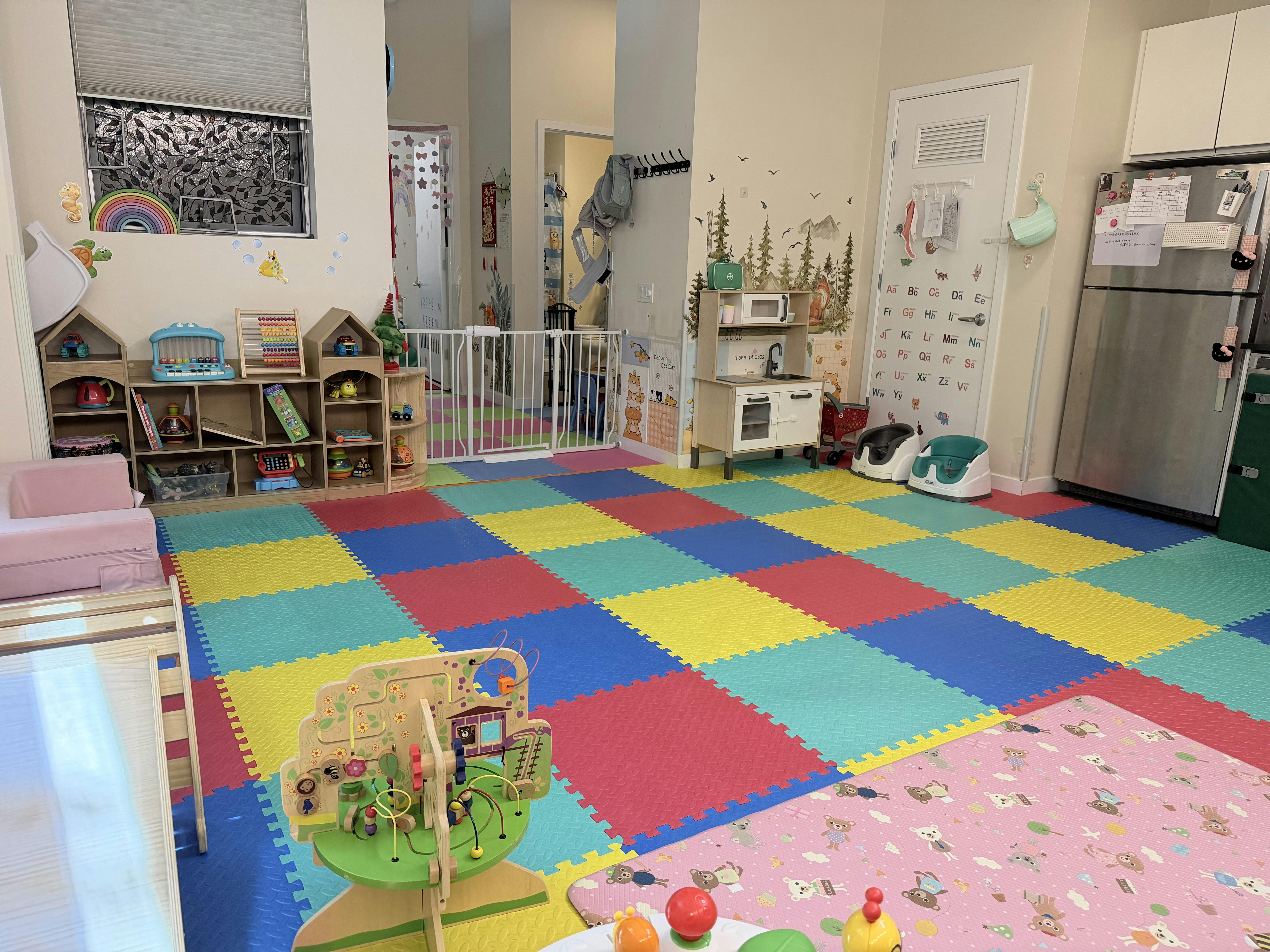 Childcare room with colorful floor mats, toy shelves, and a play kitchen
