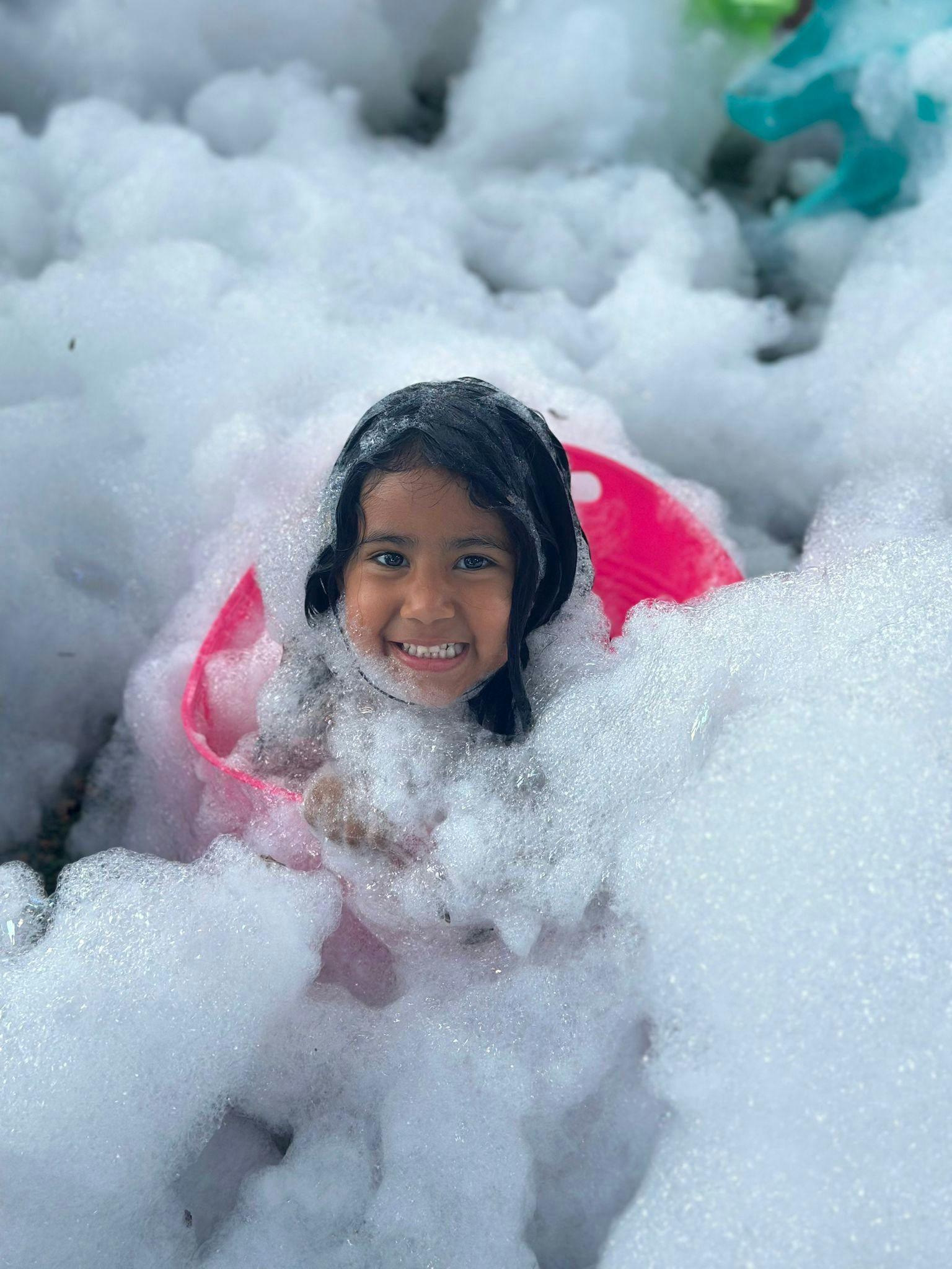 Child in a pink bucket surrounded by foam