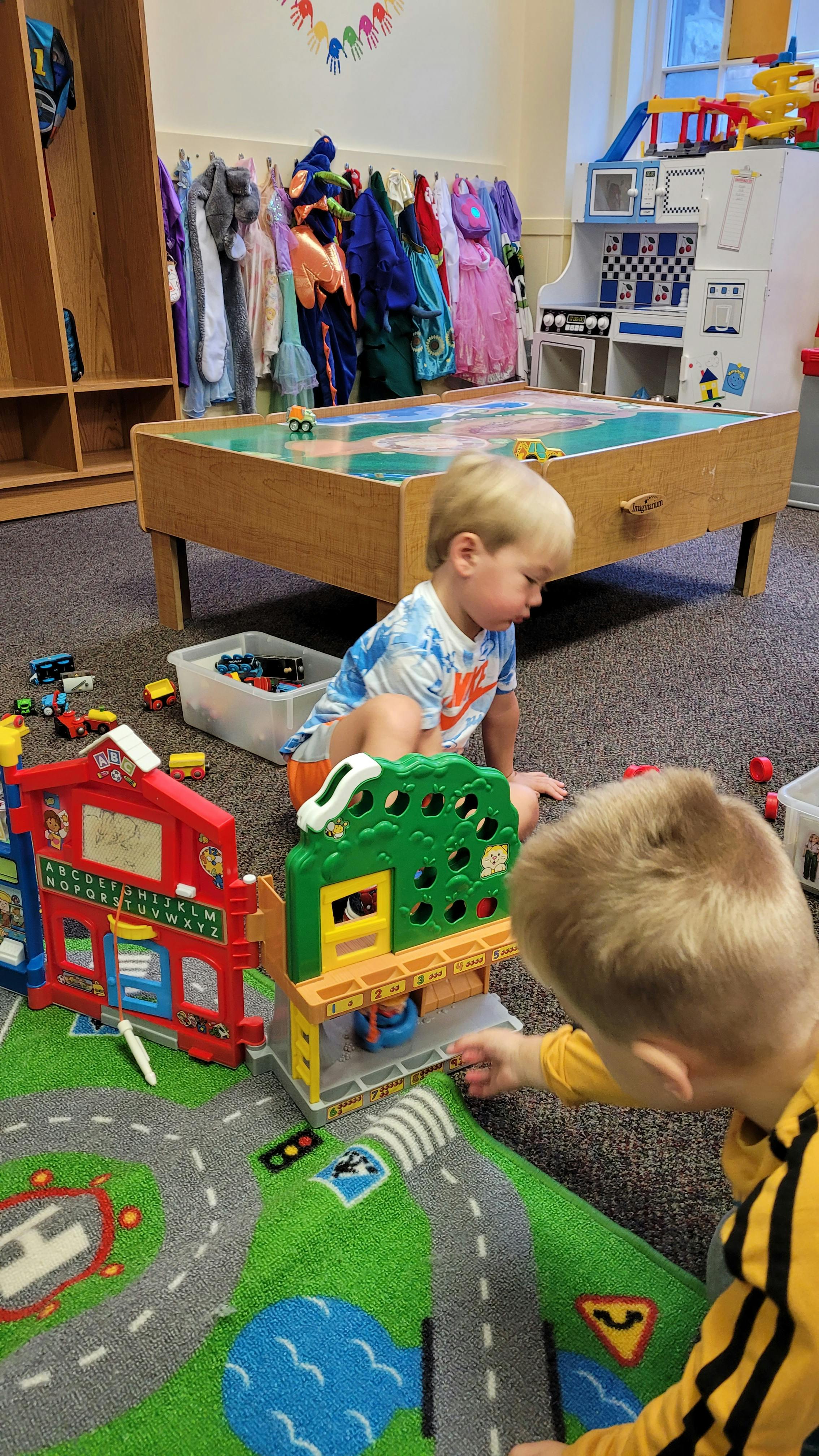 Two children playing with toys on a road-themed rug in a classroom