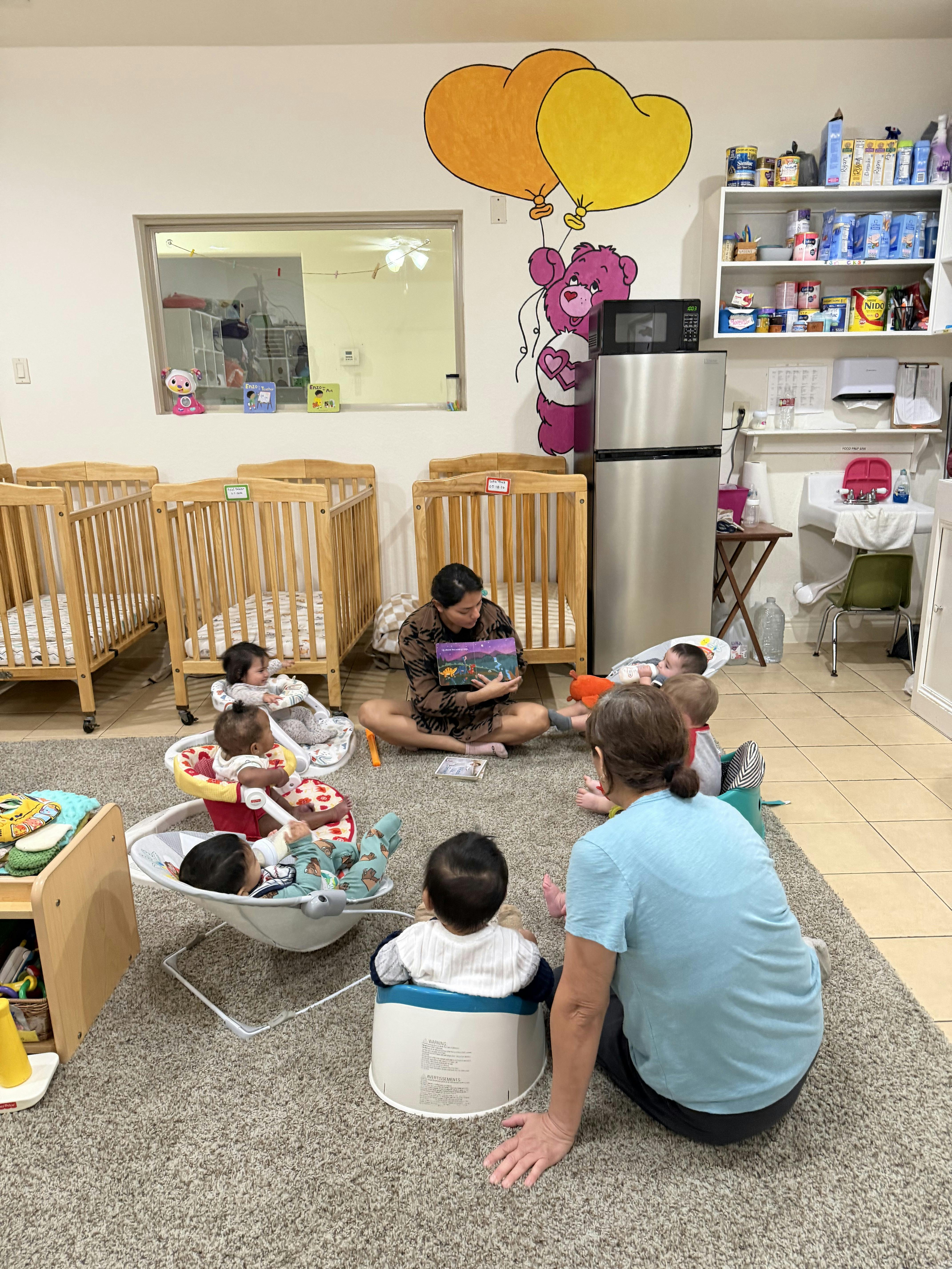 Adults sitting on a rug reading a book to infants in a daycare classroom