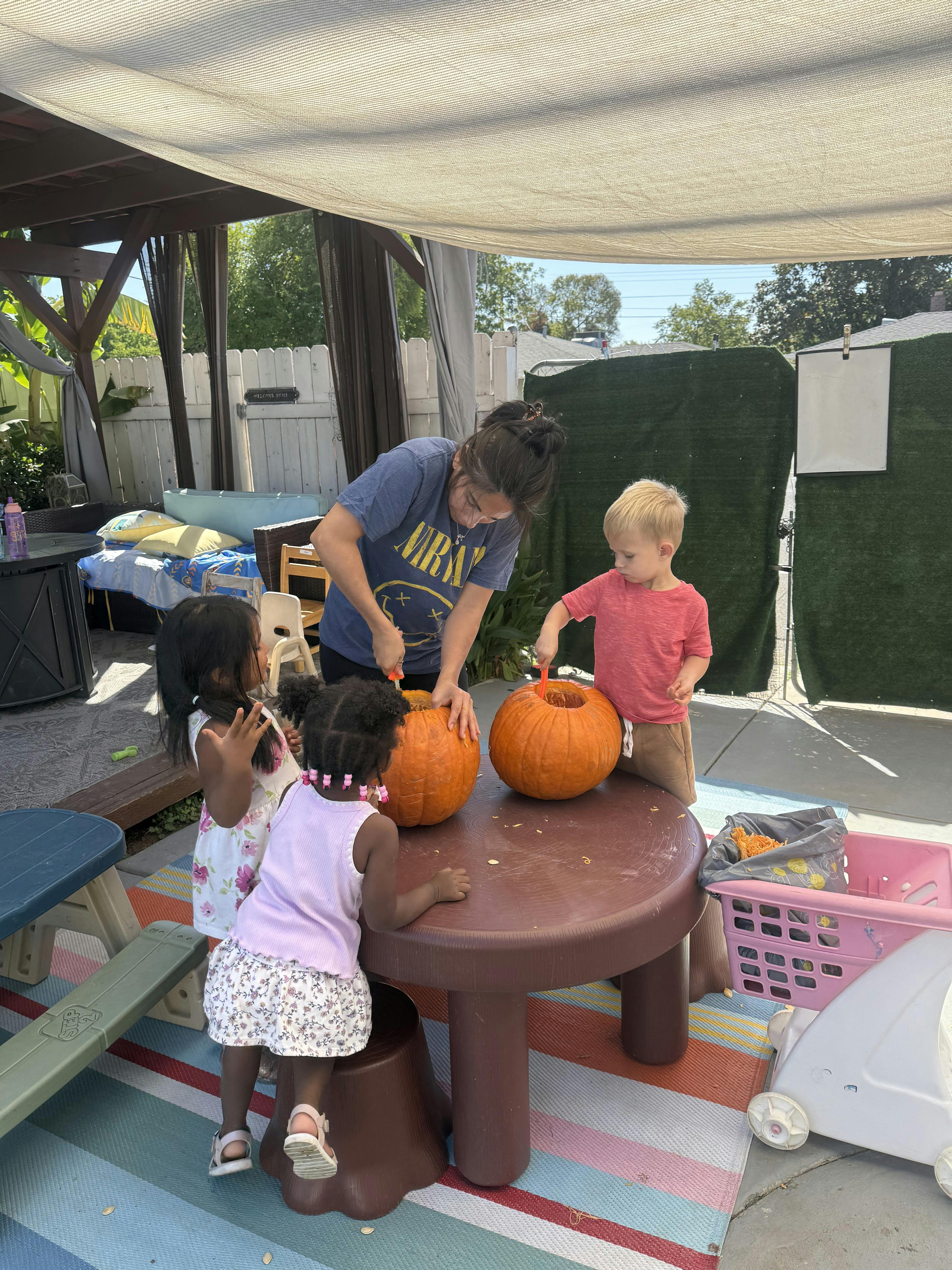 A person and three children scooping out the inside of pumpkins on a table