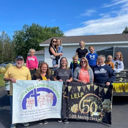 Group of adults and children holding two banners for Little Esko Lutheran Preschool