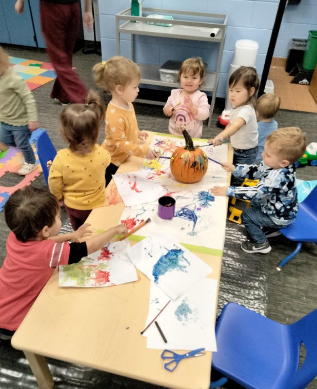 Children painting a pumpkin and paper at a table