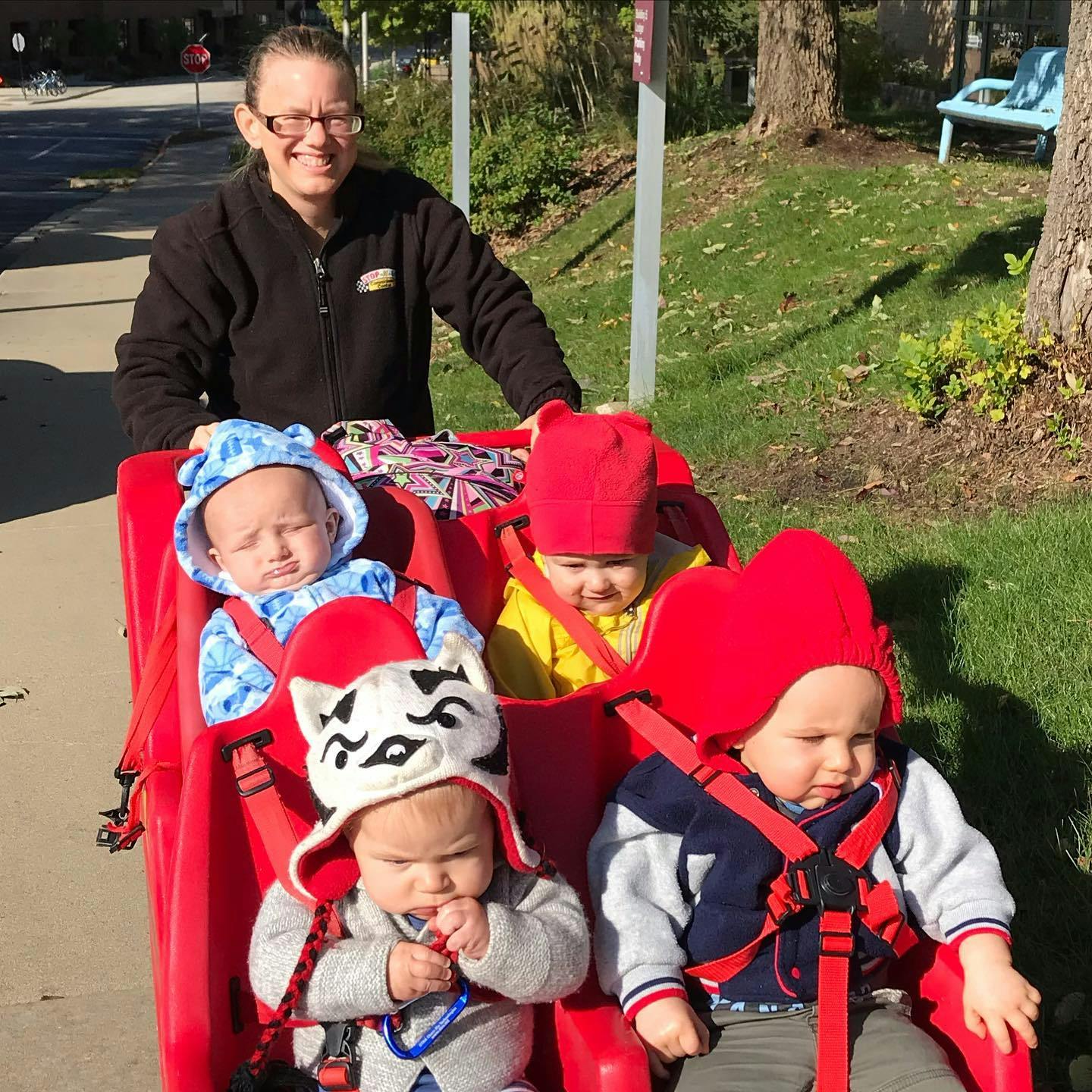 Person pushing multiple children in a red stroller