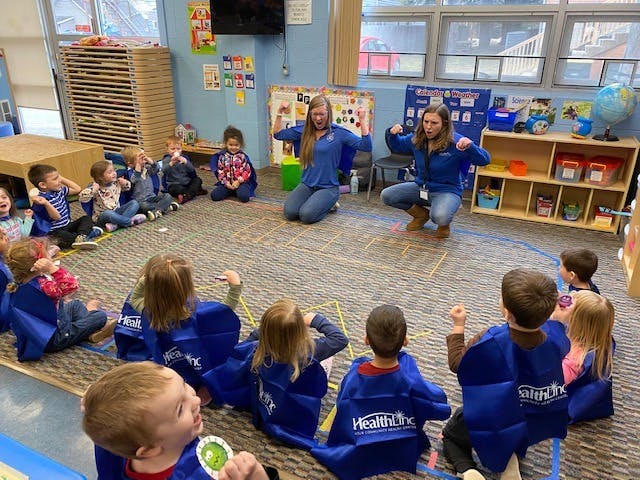 Two people leading a group of children in an activity in a classroom