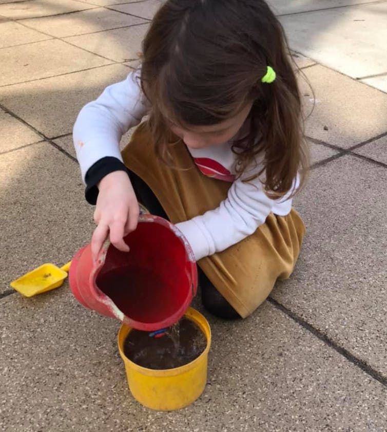 Child pouring water from a red cup into a yellow pot