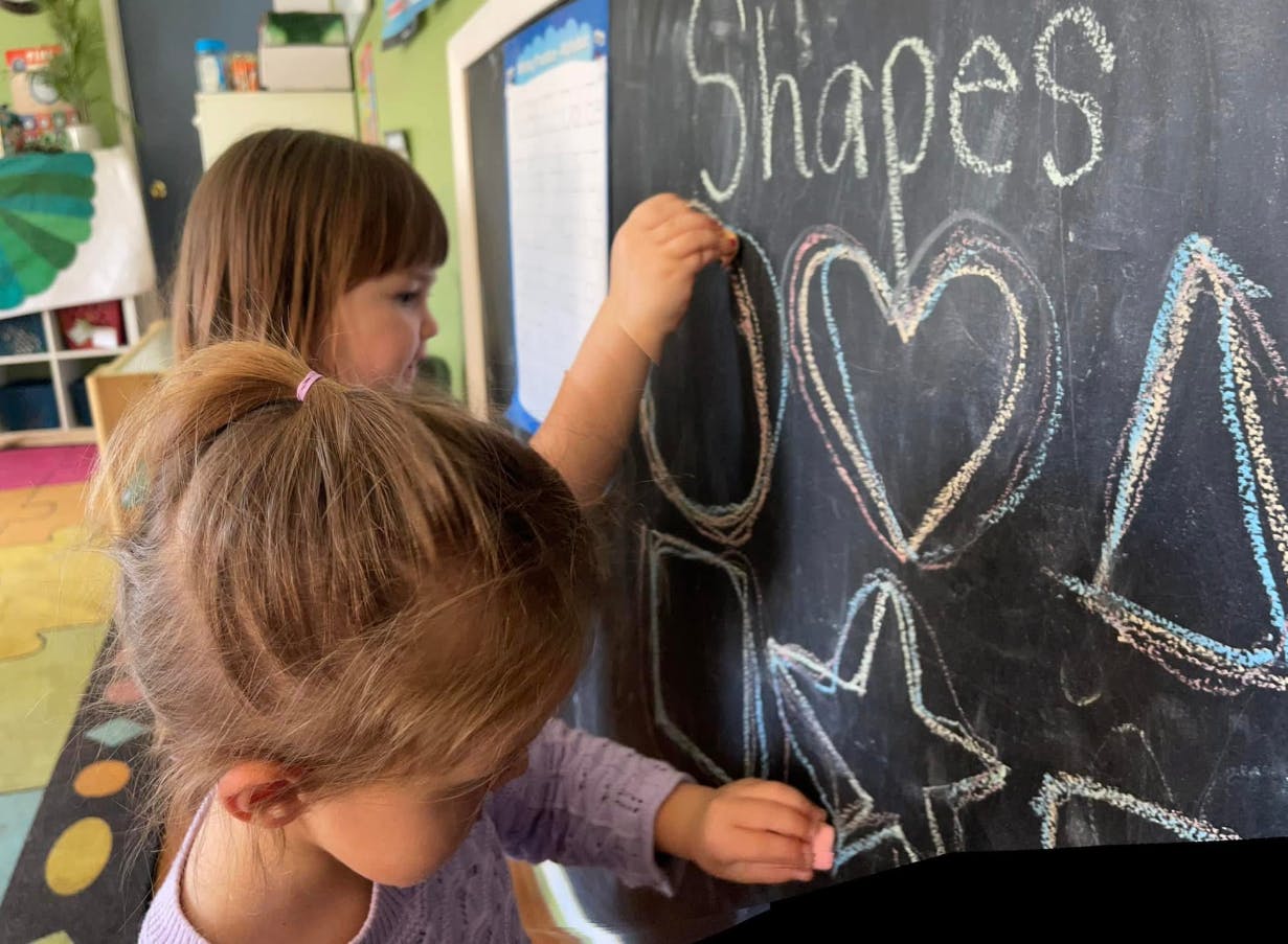 Two children drawing shapes on a chalkboard