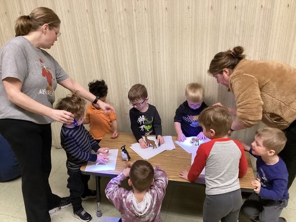 Two people helping several children with an activity at a table