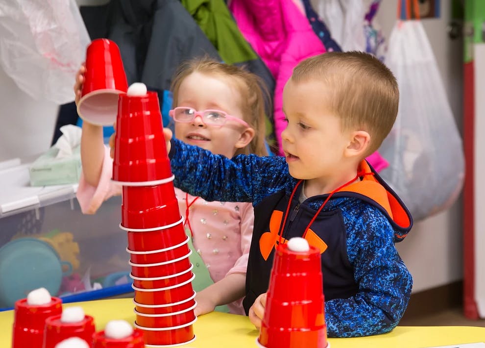 Two children stacking red cups with white balls on top