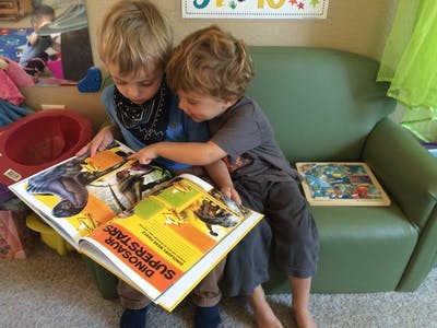 Two children sitting on a couch reading a book together