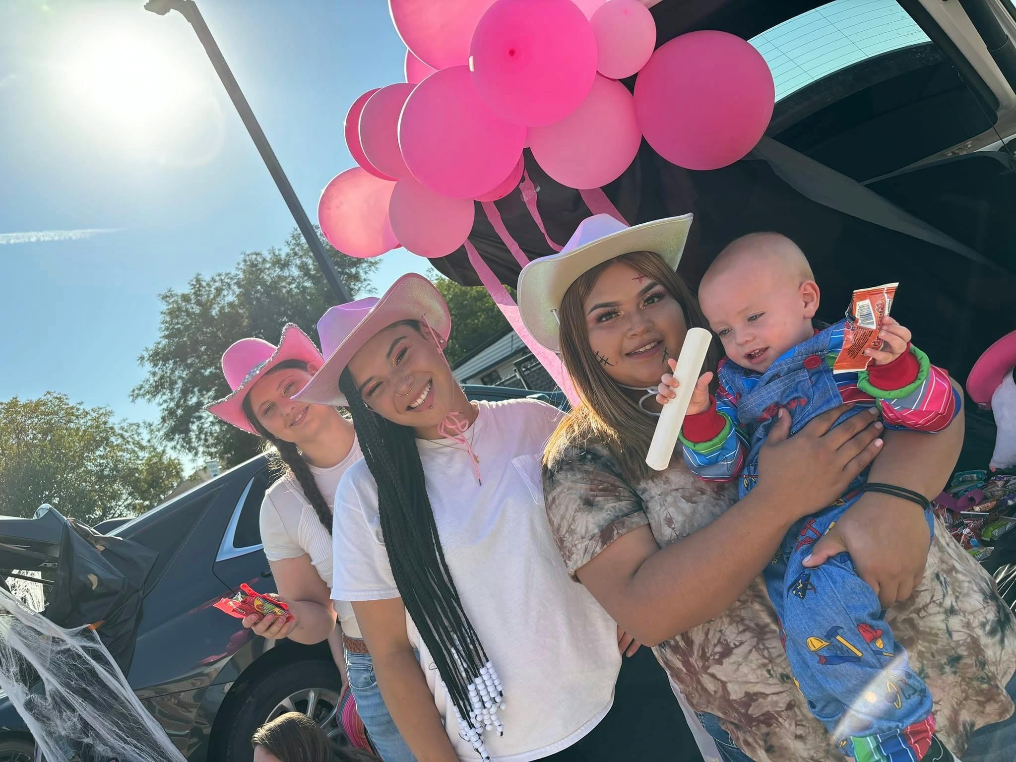 Three people in cowboy hats with a child, pink balloons in background