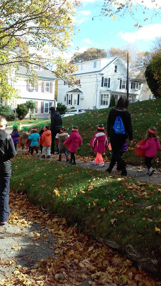 Adults and children walking on a sidewalk with autumn leaves
