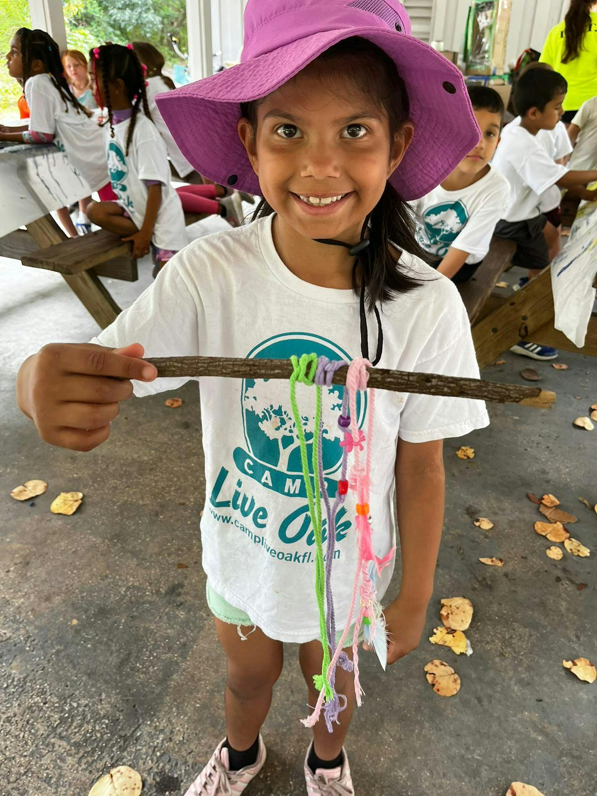 Child in a purple hat holding a stick with colorful strings tied to it