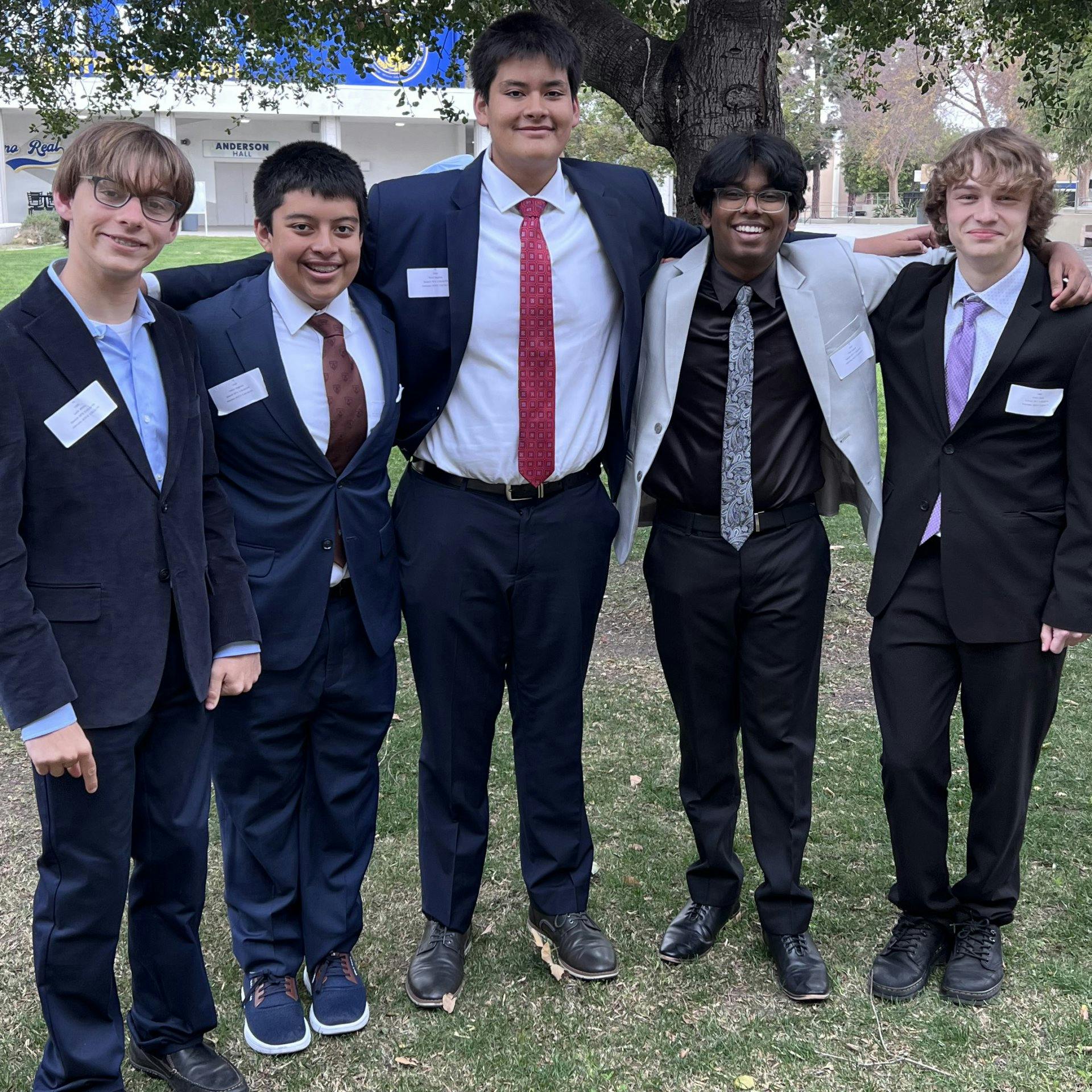 Five teens in suits and ties standing together outdoors