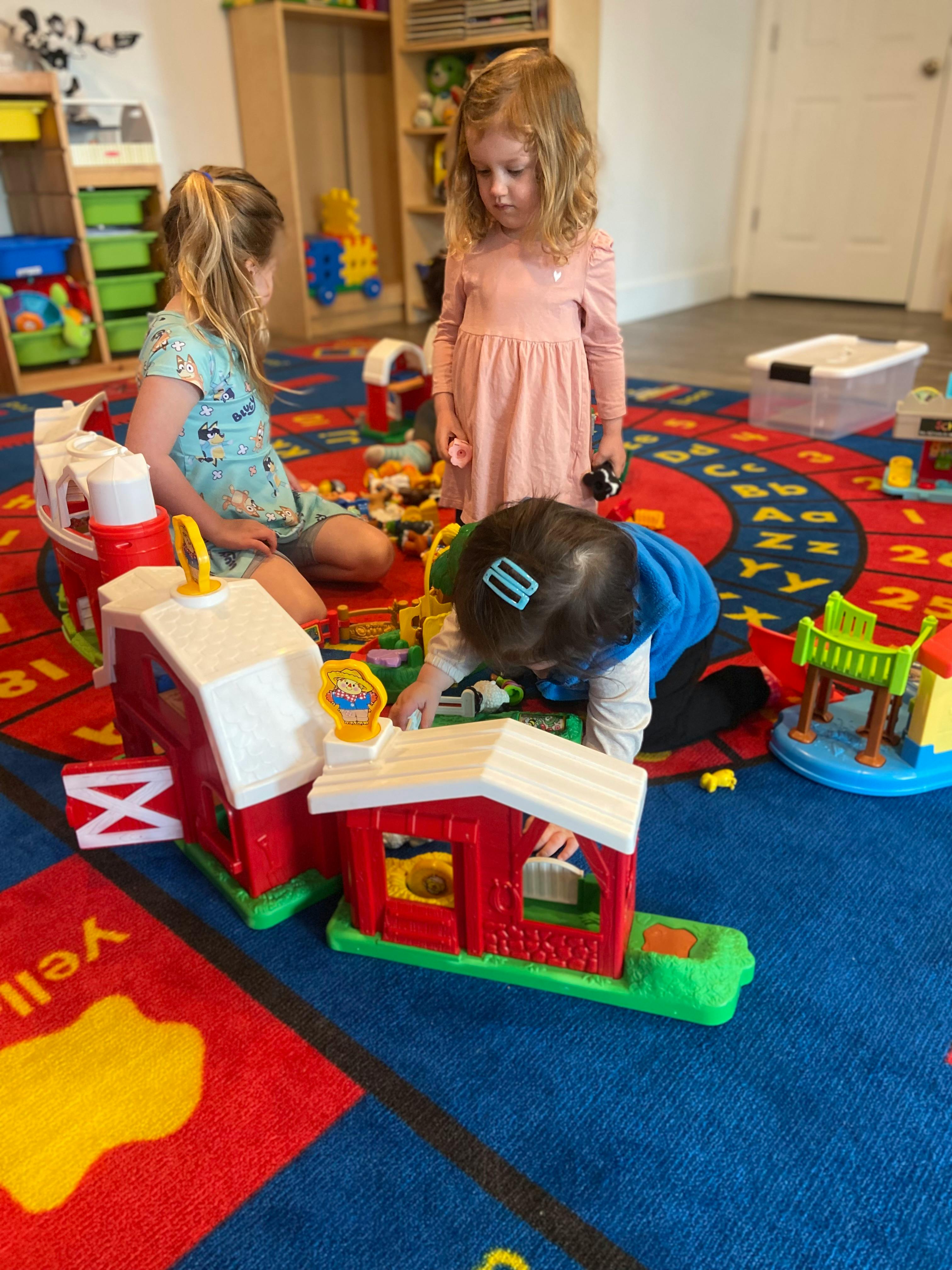 Three children playing with toy barns on a colorful rug