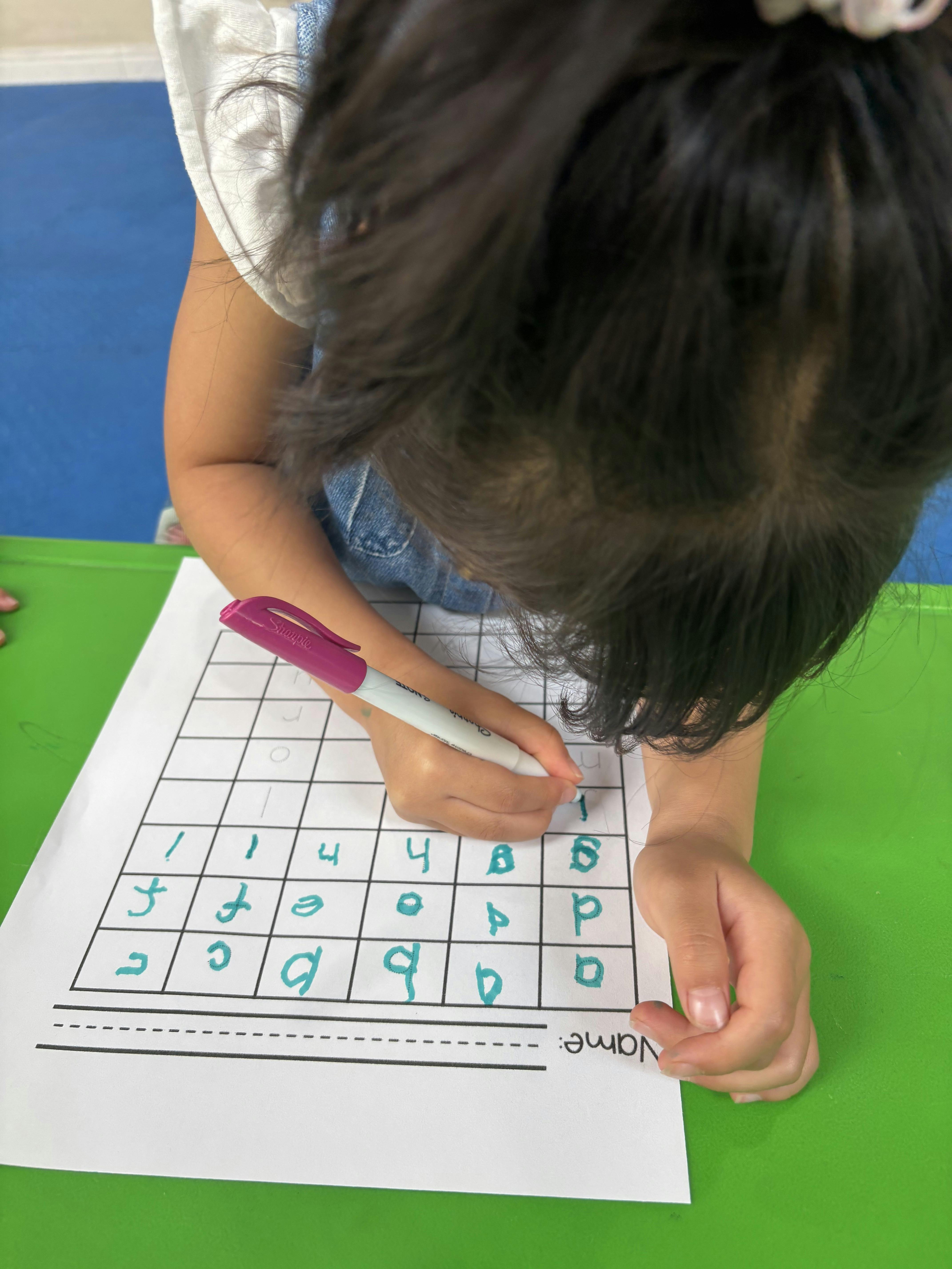 Child writing letters and numbers on a worksheet with a marker