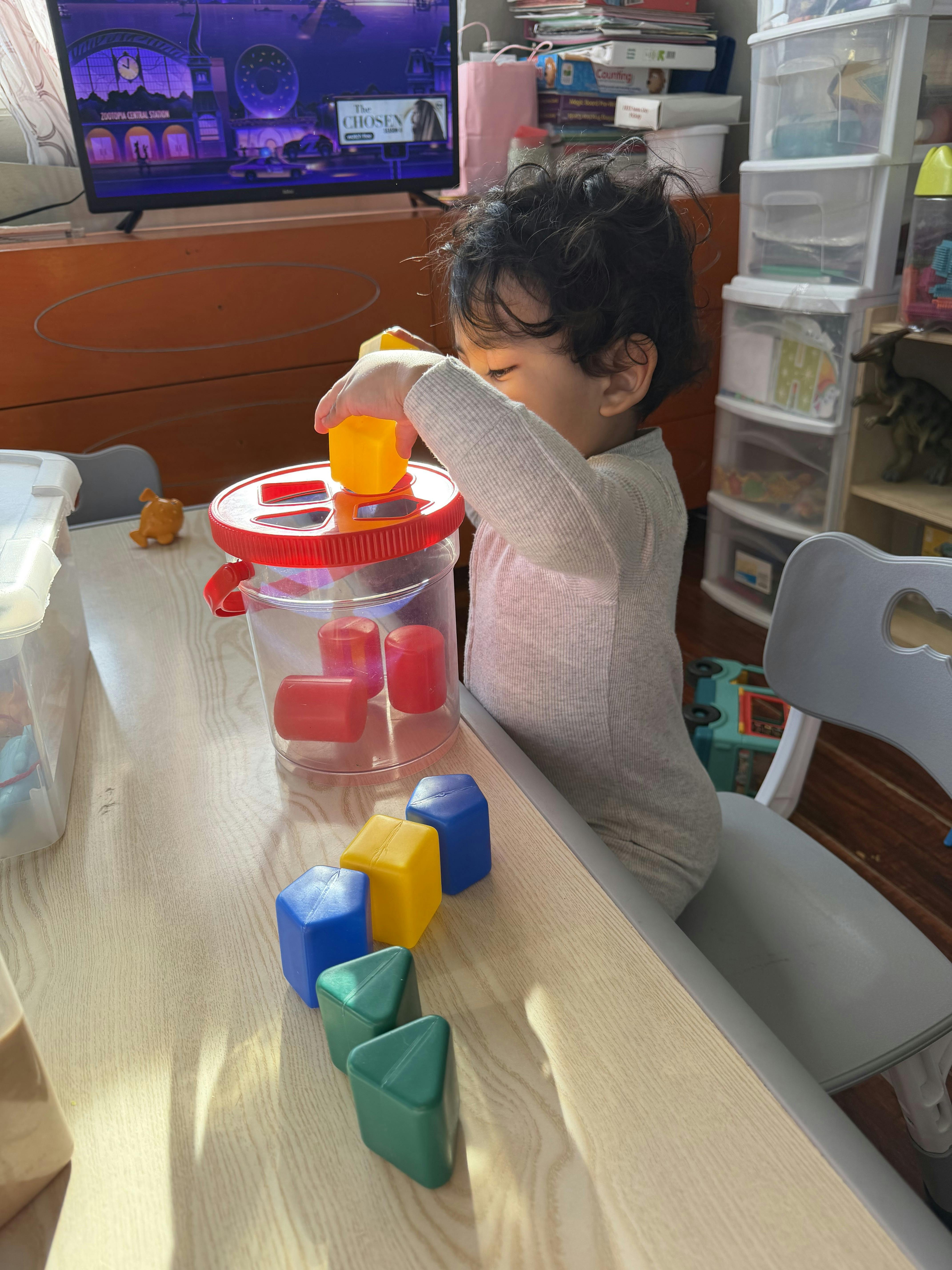 Child putting a yellow block into a shape sorter on a table
