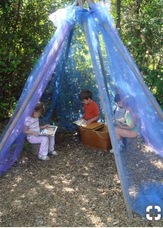 Three children reading books inside a blue mesh tent outdoors