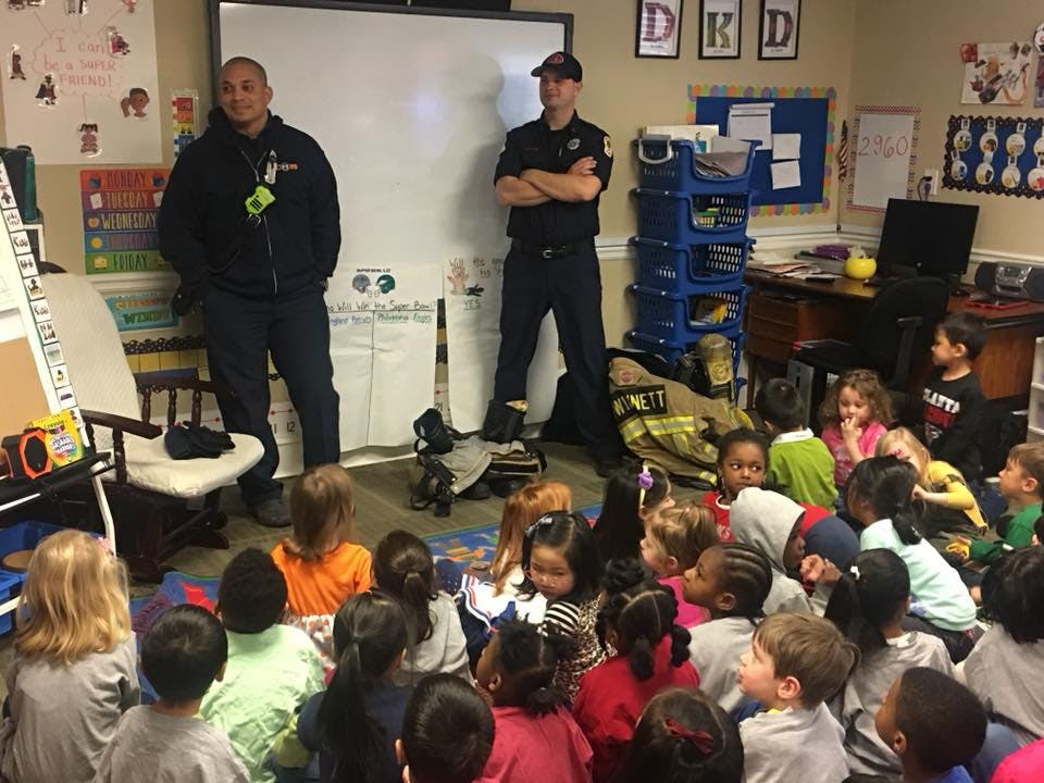 Two people in uniform standing in front of children sitting on the floor