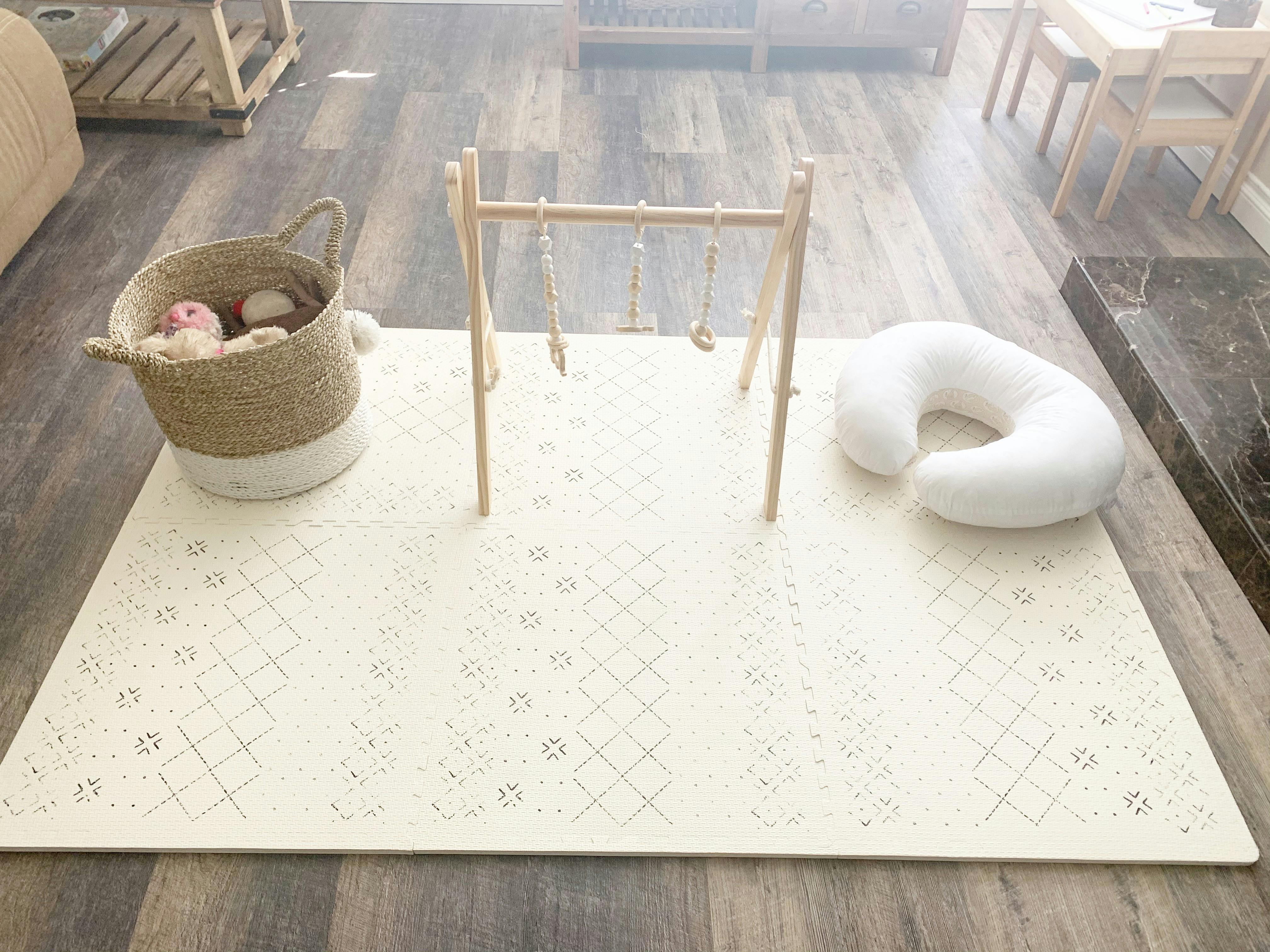 Play mat with a wooden baby gym, basket of toys, and nursing pillow