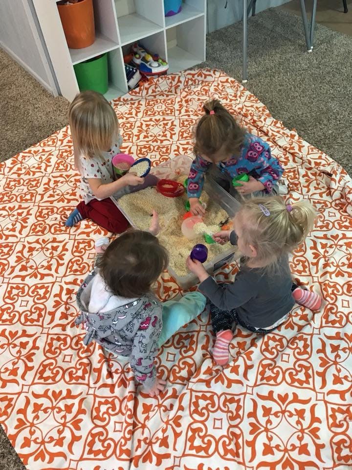 Four children playing with sand and toys on a patterned blanket
